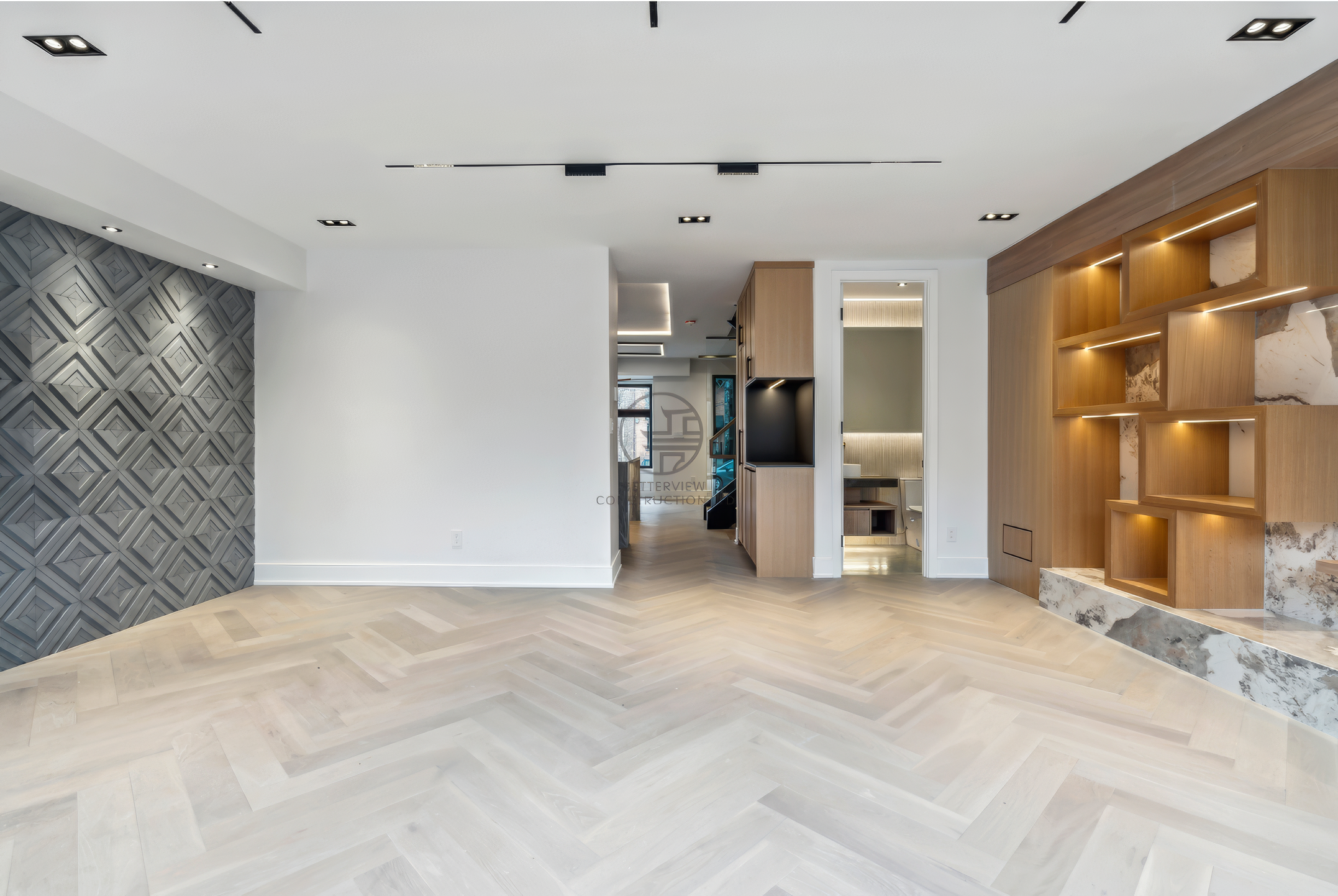 Modern open-concept living space with herringbone wood flooring, feature wall, custom built-in shelving, and recessed lighting in a luxury home renovation project