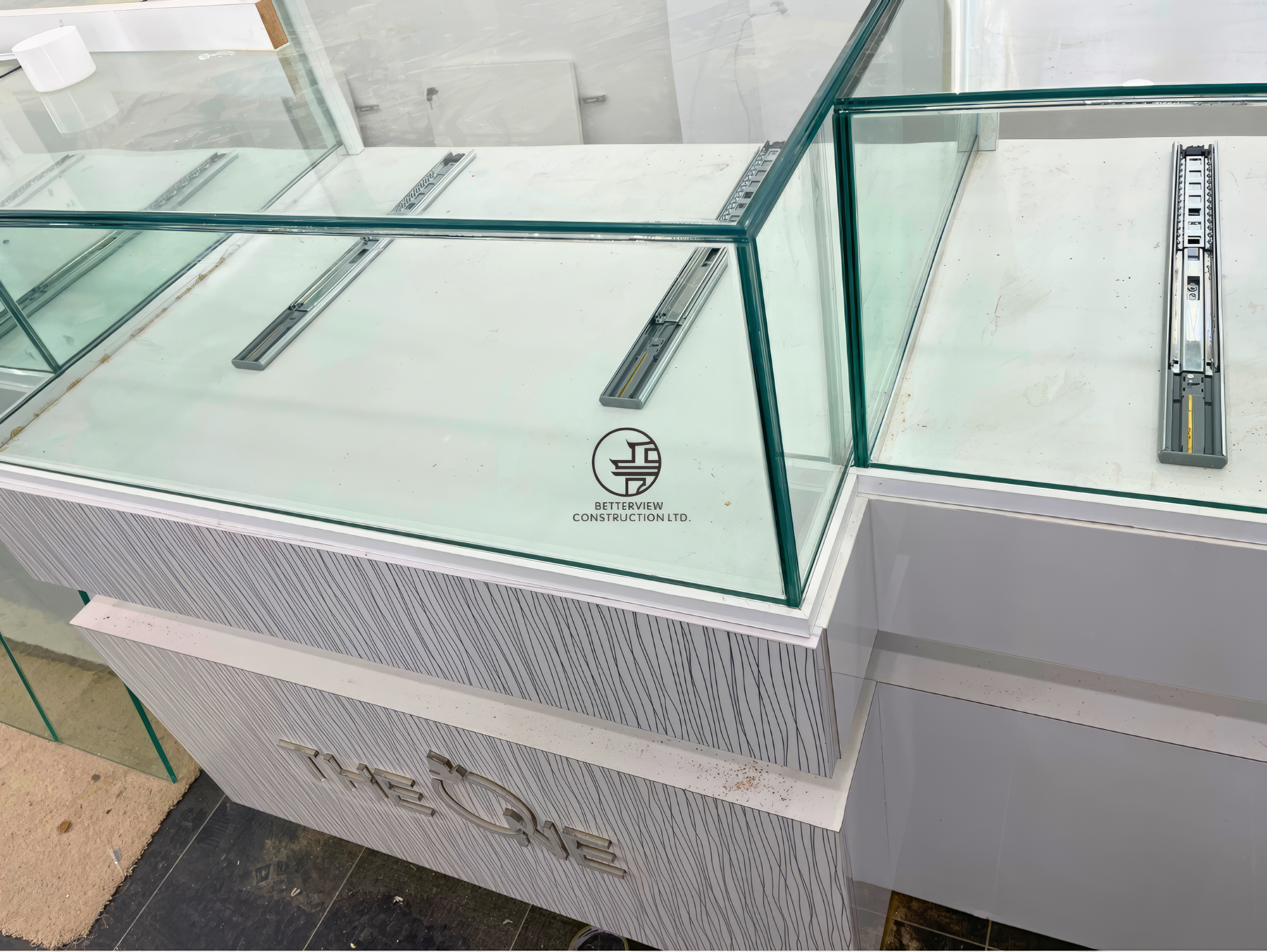 Close-up of custom glass display counter installation with metal tracks and base cabinetry in retail renovation project