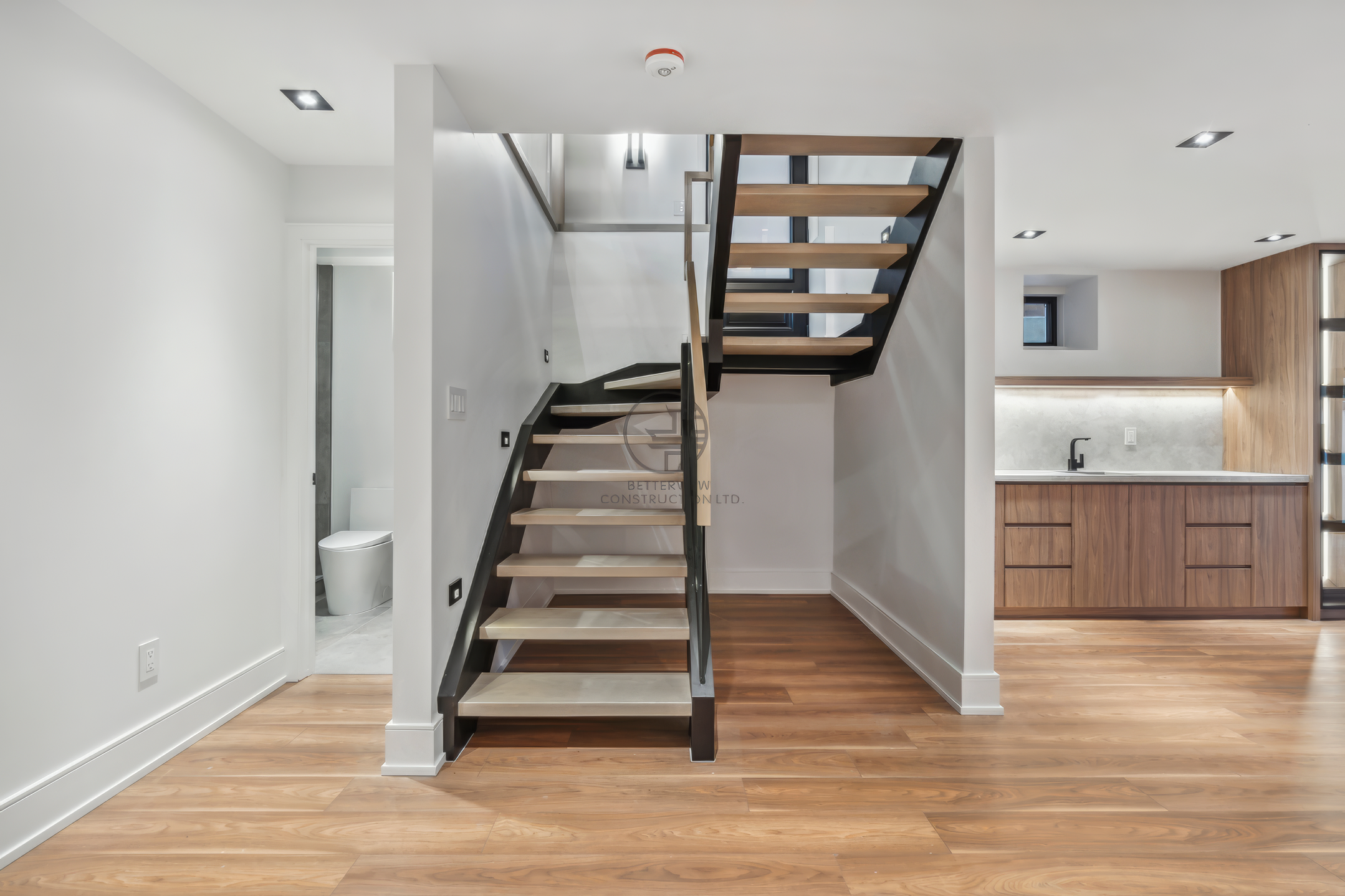 Modern interior with floating staircase, wood flooring, open-concept layout, and built-in cabinetry in a residential home renovation project