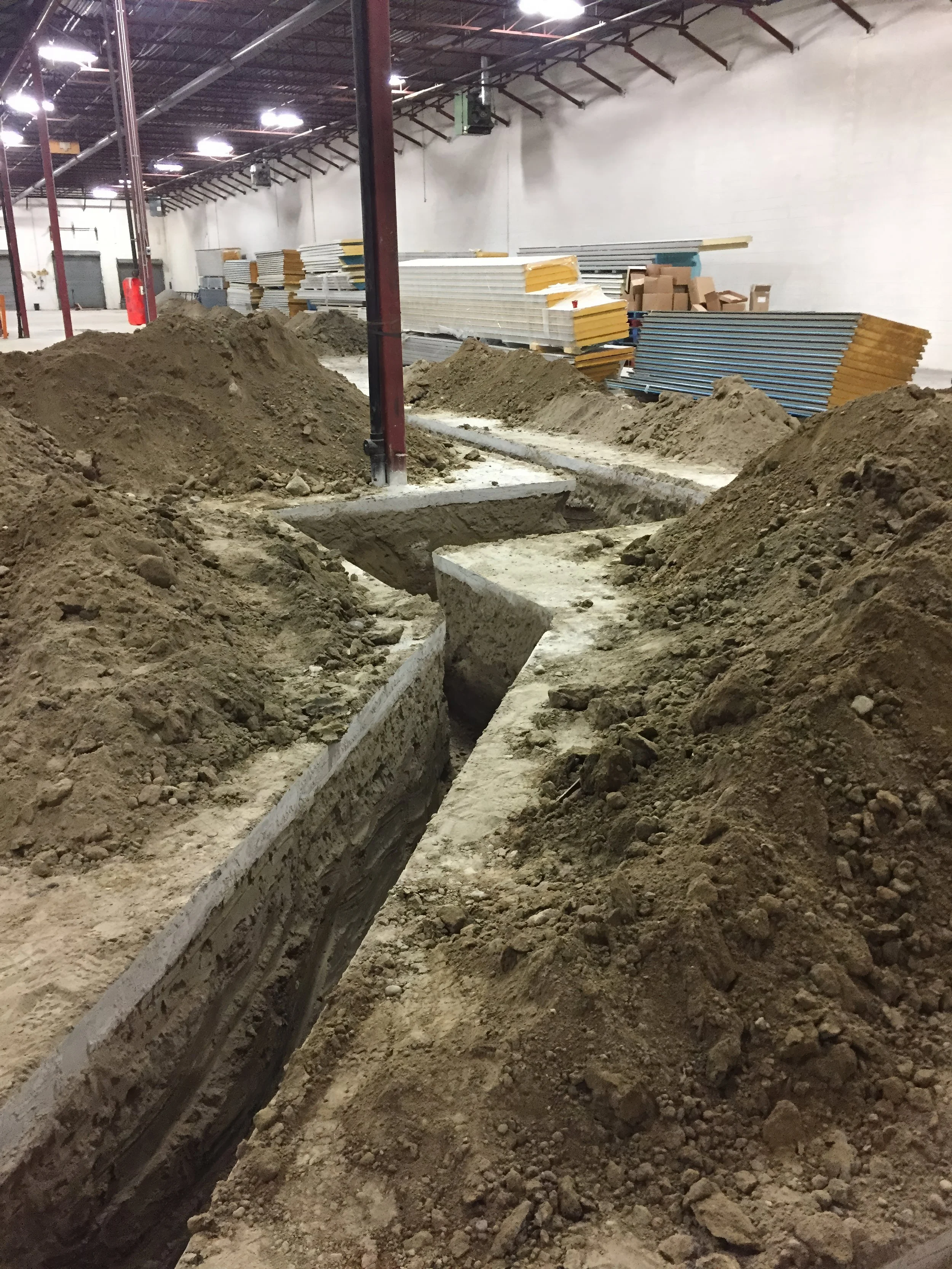Commercial construction site with deep trenching and foundation excavation work inside a warehouse during renovation in Toronto