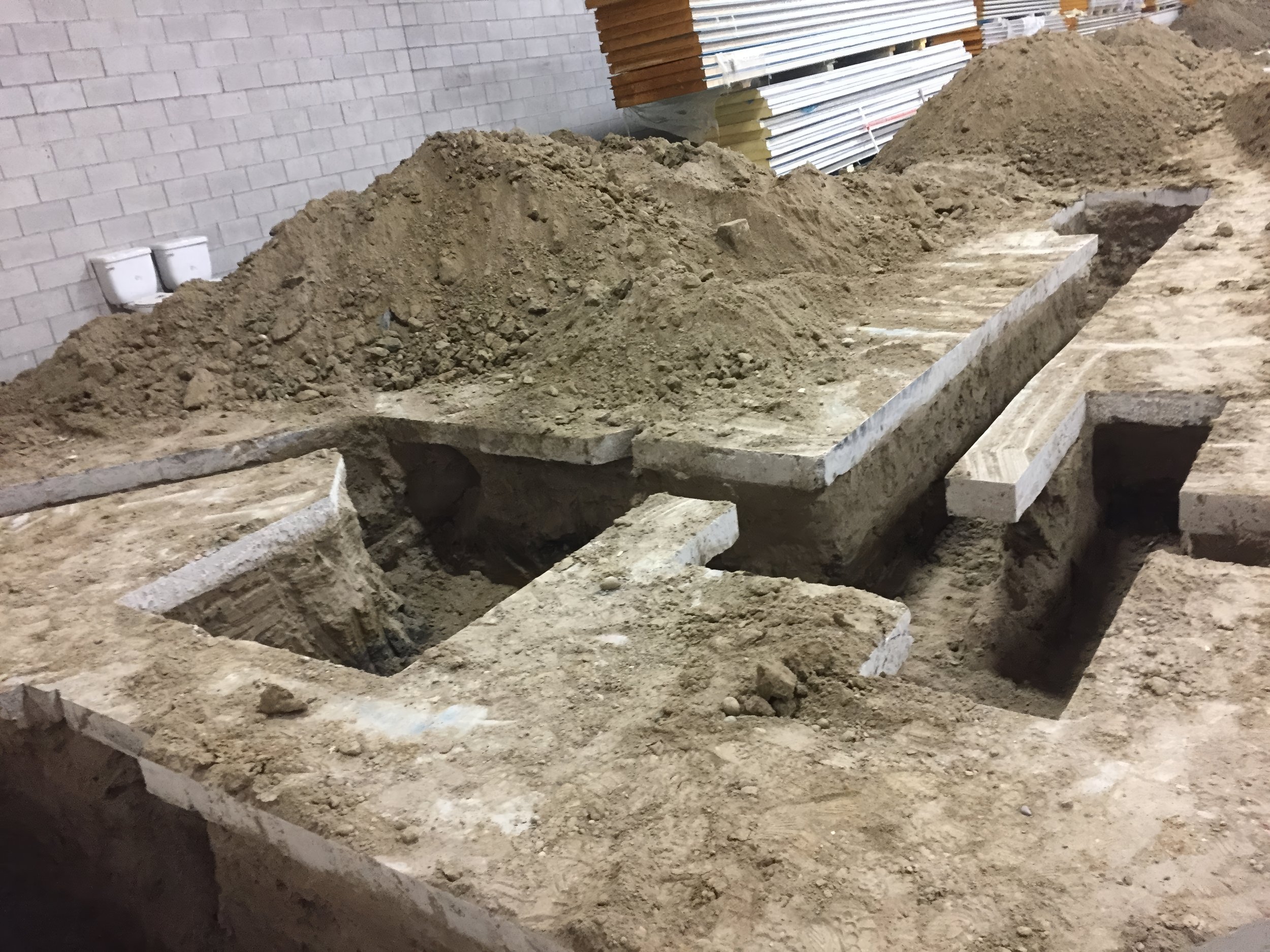 Commercial interior construction showing deep foundation excavation, concrete slab cutting, and trenching work for structural and plumbing preparation in Toronto