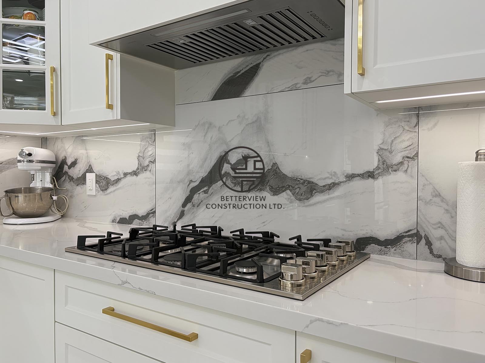 The custom cooking area features a professional gas cooktop, concealed range hood, quartz countertops, and a dramatic marble-look backsplash for a clean, luxurious finish.