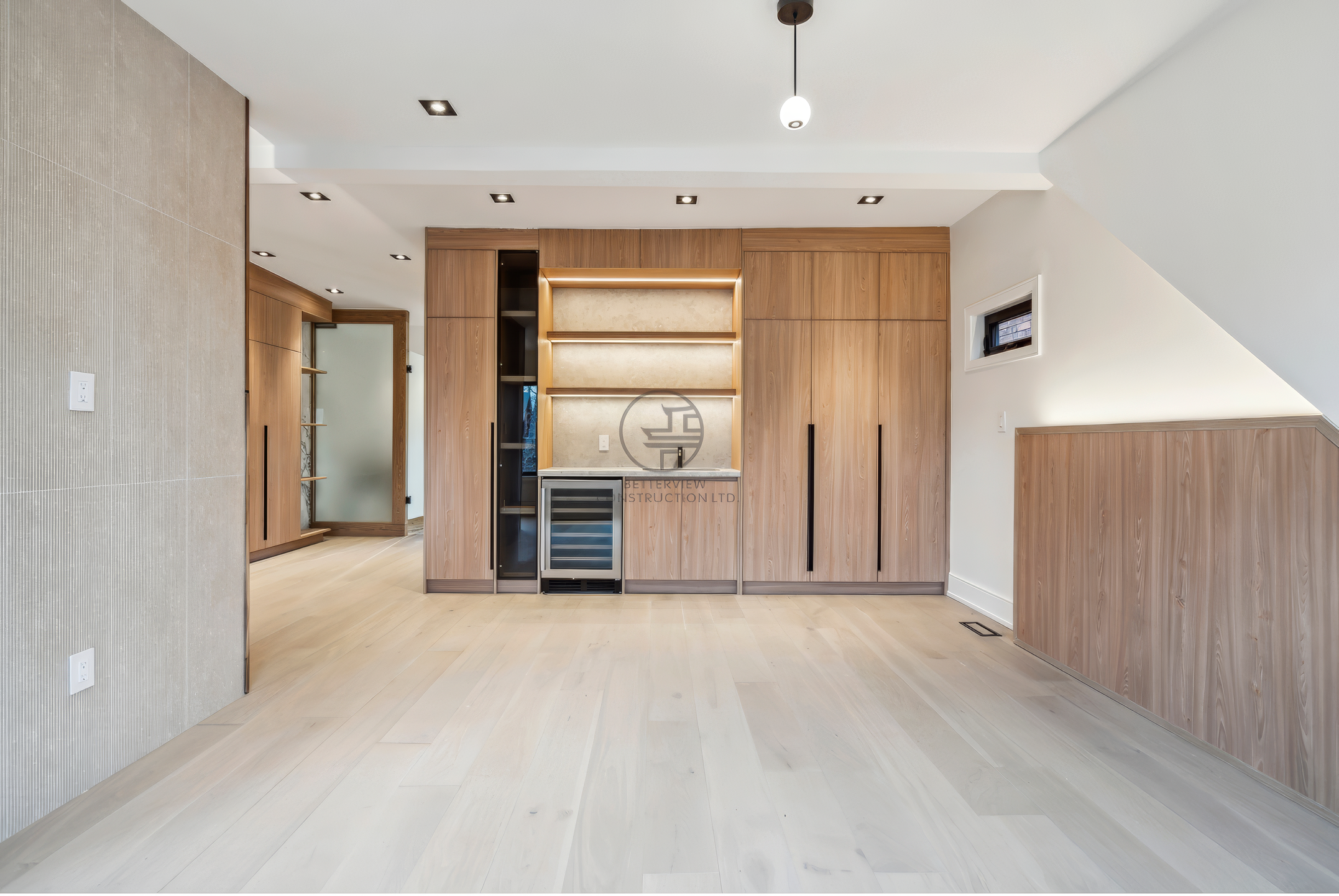 Modern open-concept living space with custom wood cabinetry, built-in shelving, wine fridge, and recessed lighting in a luxury home renovation project