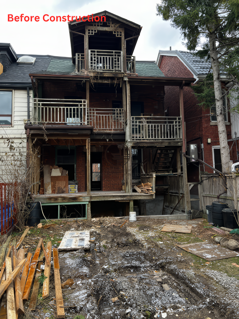 Before construction rear view of residential home with old wooden decks, deteriorating structure, and unfinished backyard in a full home renovation project