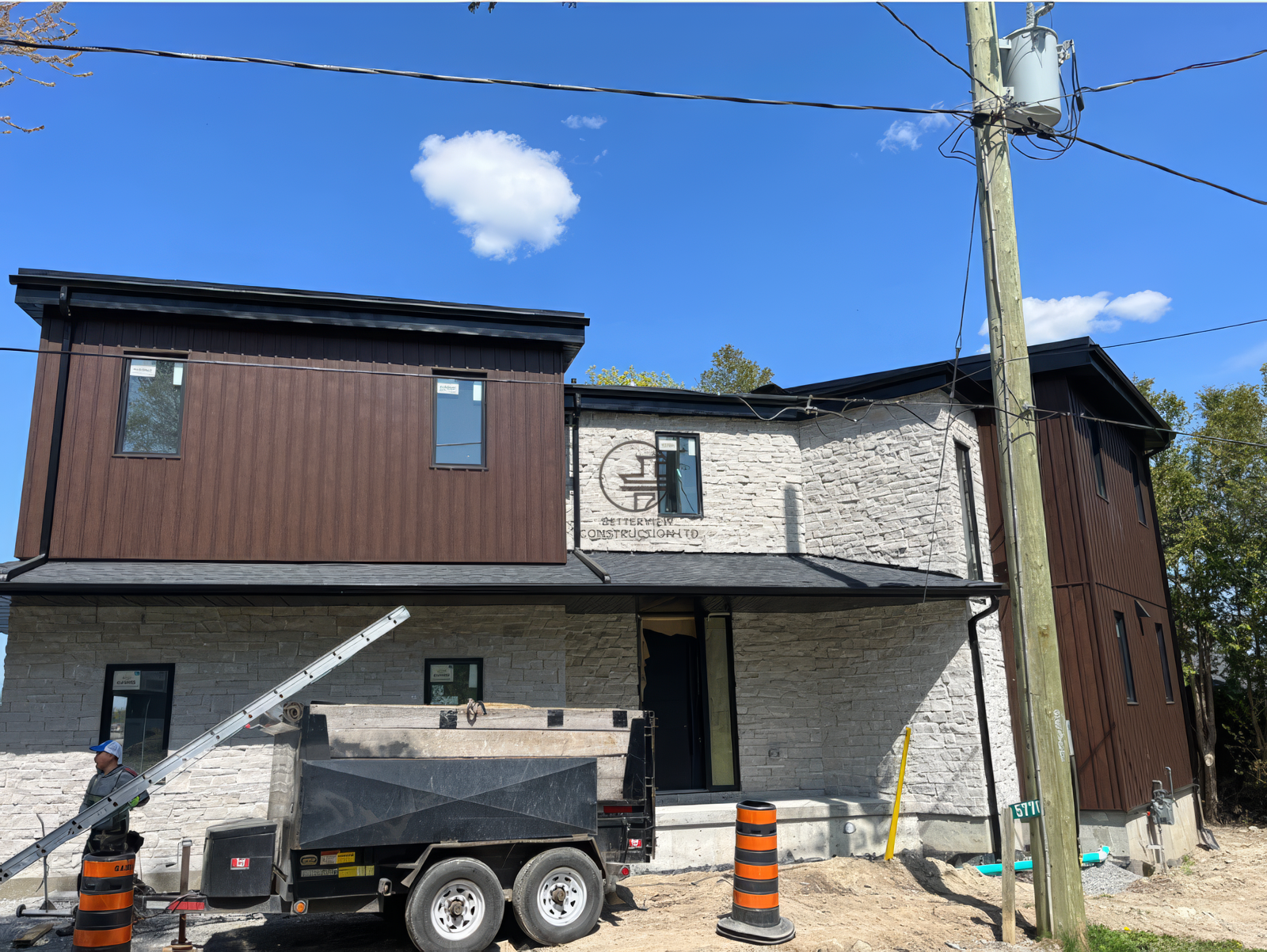 Modern home exterior renovation with stone facade and wood siding, construction nearing completion with equipment on site
