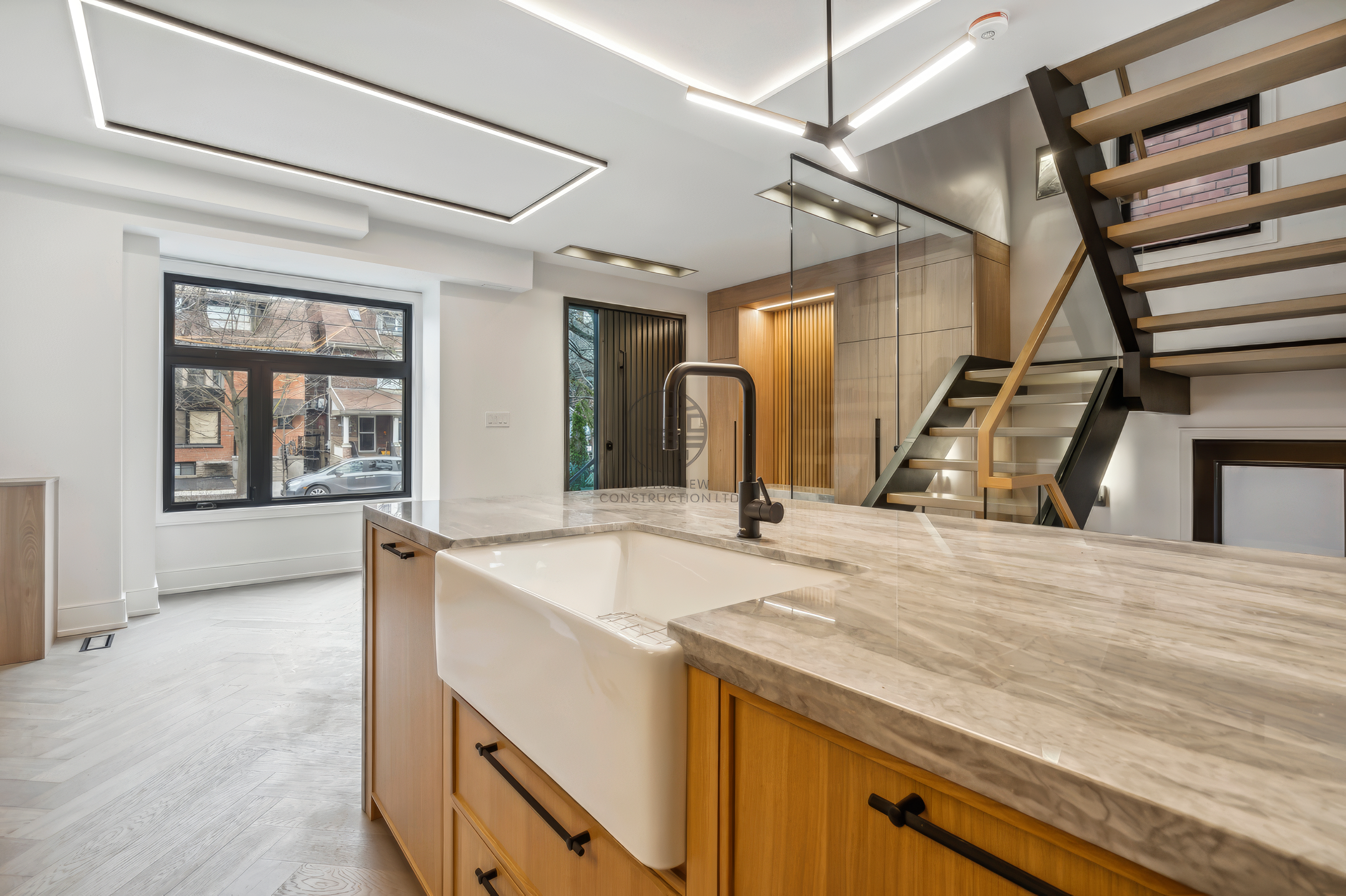 Open-concept kitchen and living space with large island, farmhouse sink, modern staircase, recessed lighting, and hardwood flooring in a luxury home renovation project