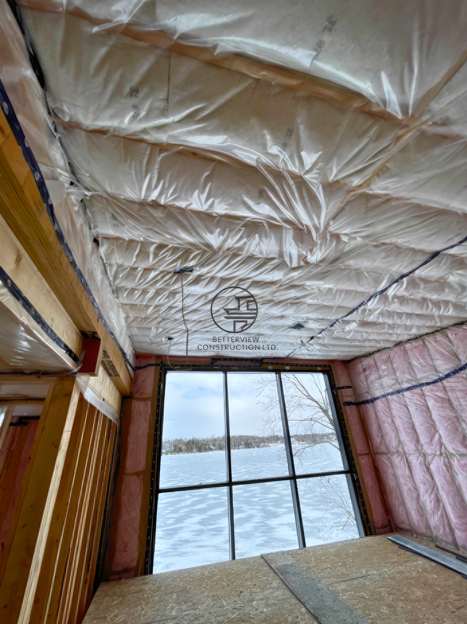 Interior construction framing with spray foam insulation on ceiling and walls, large window view, home renovation in progress
