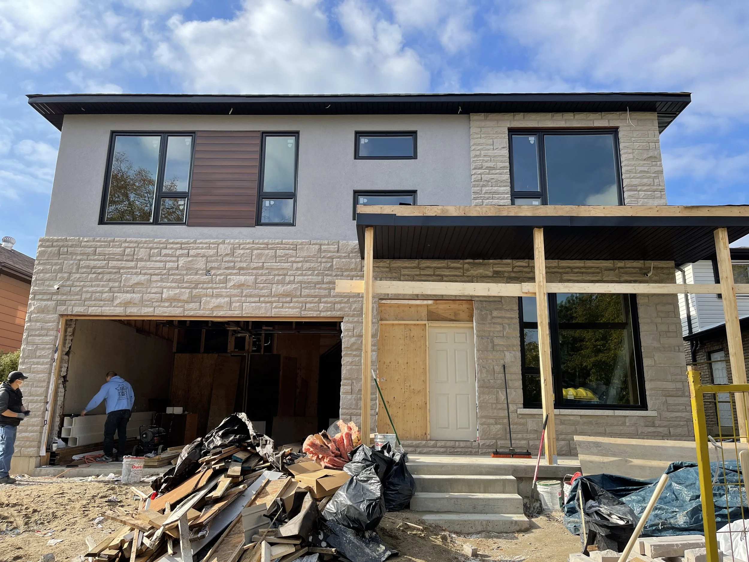 Modern front elevation featuring a completed over-the-garage addition with stone veneer, large windows, and a covered front porch during the final stages of construction.