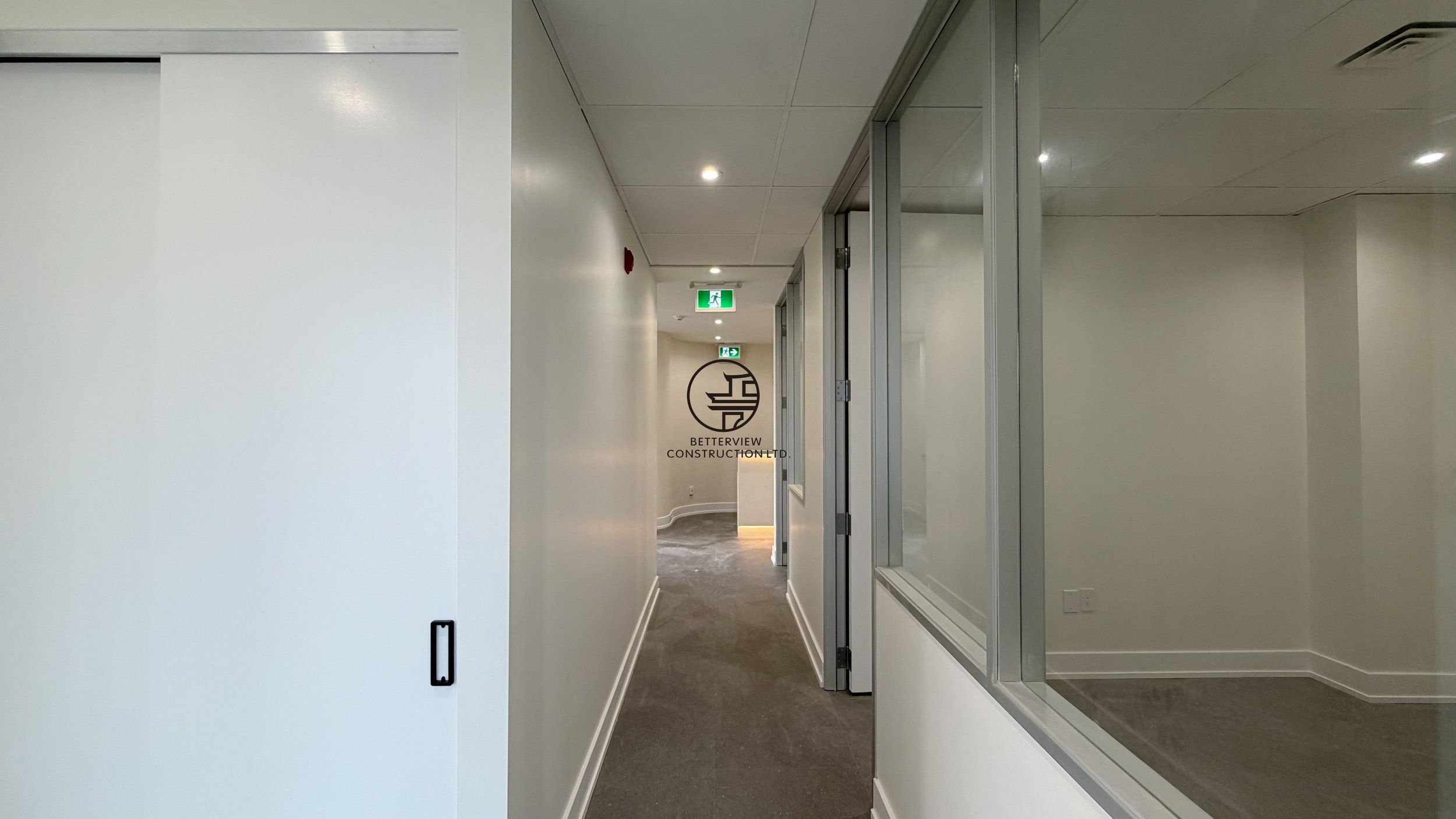 Modern office hallway with sliding door, interior window, and recessed lighting in commercial renovation