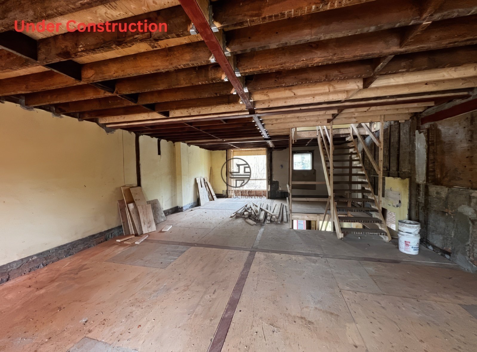 Under construction interior with exposed ceiling joists, open floor space, staircase framing, and partial flooring during residential home renovation