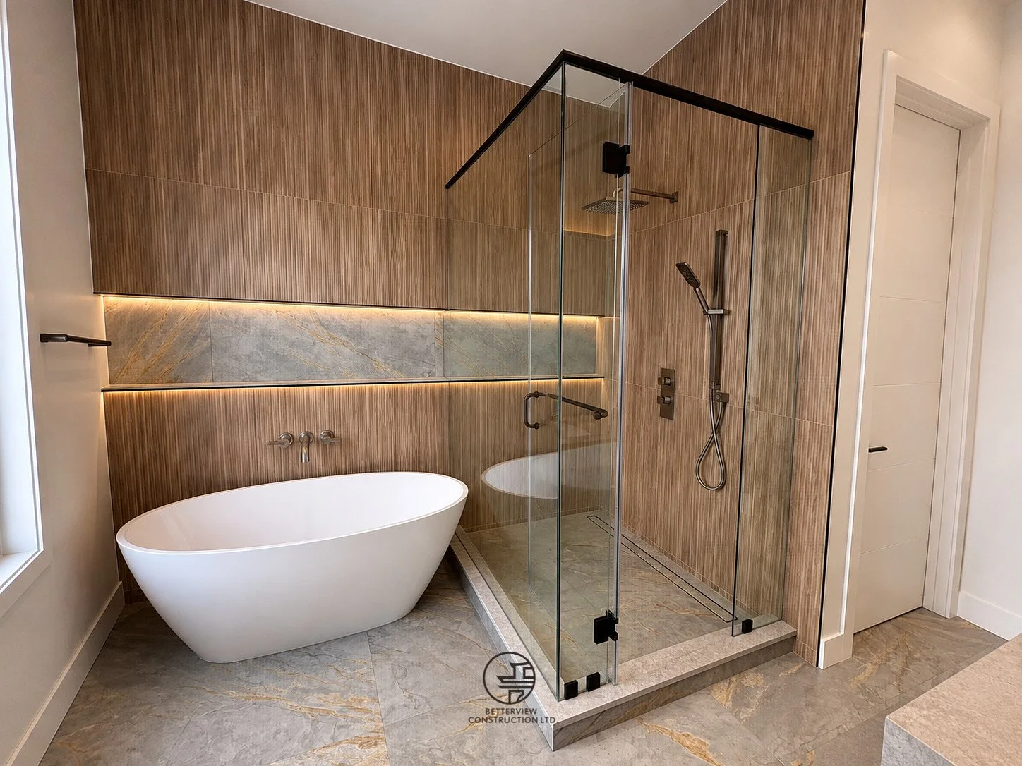 Modern bathroom featuring freestanding bathtub, glass shower enclosure, wood wall panels, marble flooring, and clean contemporary design.