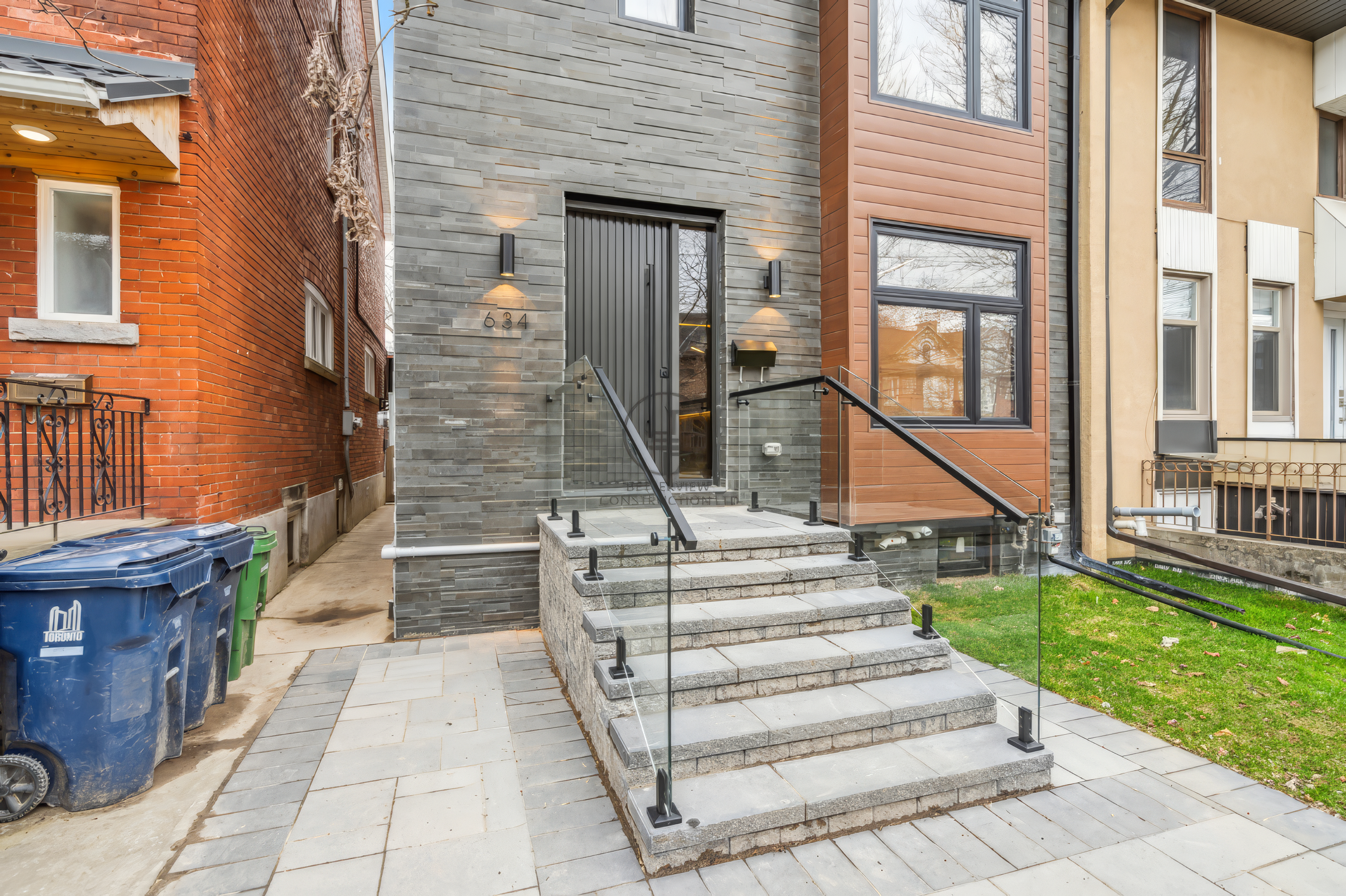 Modern home exterior with stone facade, front steps, glass railing, contemporary front door, and landscaped entry walkway.