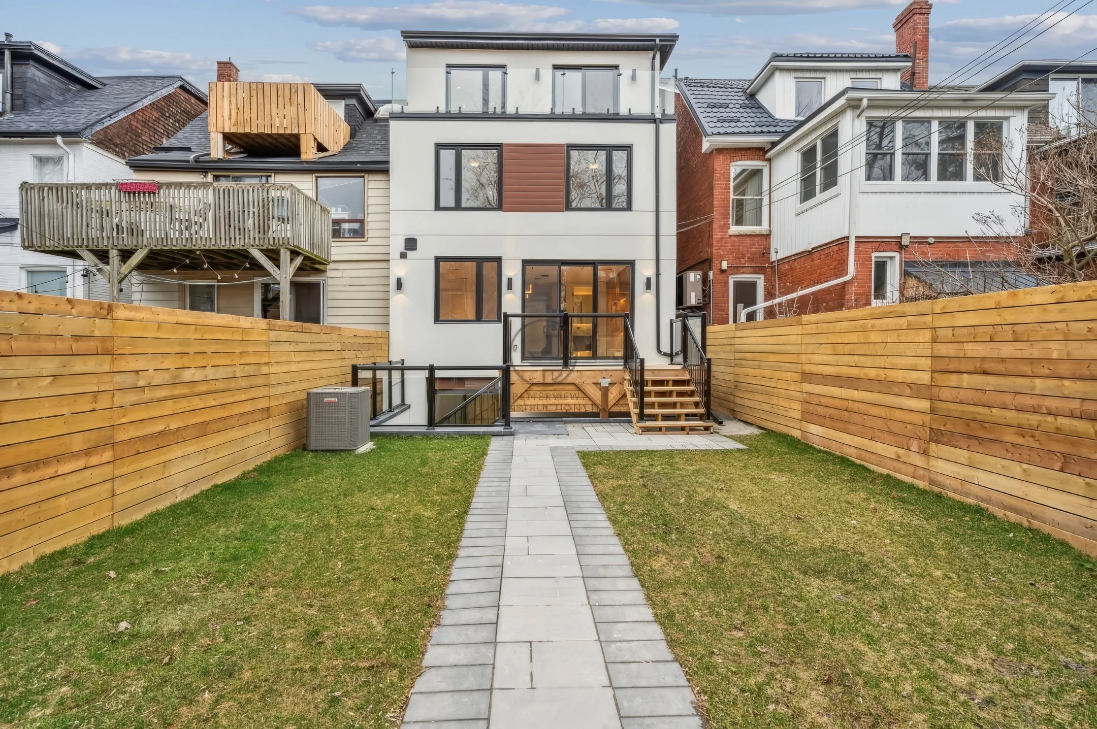 Modern custom home backyard with landscaped lawn, wooden privacy fence, stone walkway, and rear exterior view of contemporary house design.