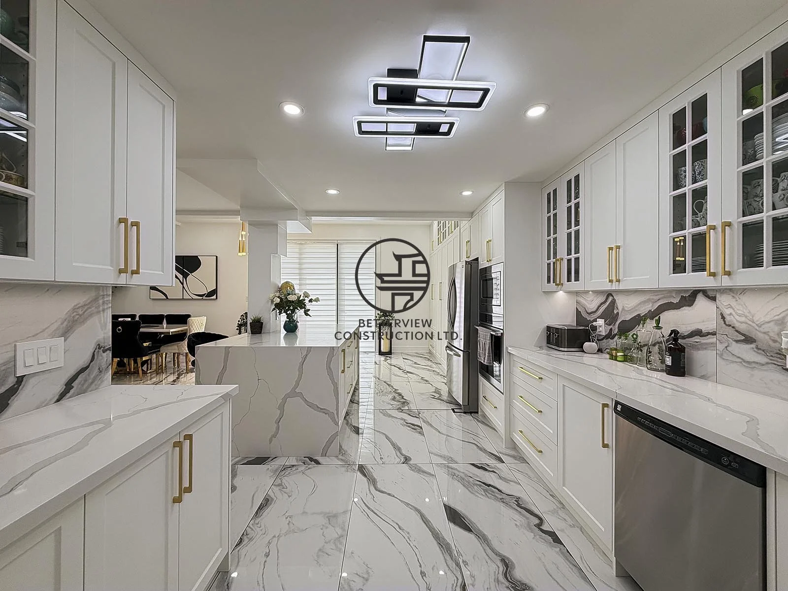 This custom kitchen renovation features full-height white shaker cabinetry, quartz countertops, a waterfall island, and a dramatic marble-look backsplash. Completed as part of a modern home addition, the space is designed to maximize storage, functio