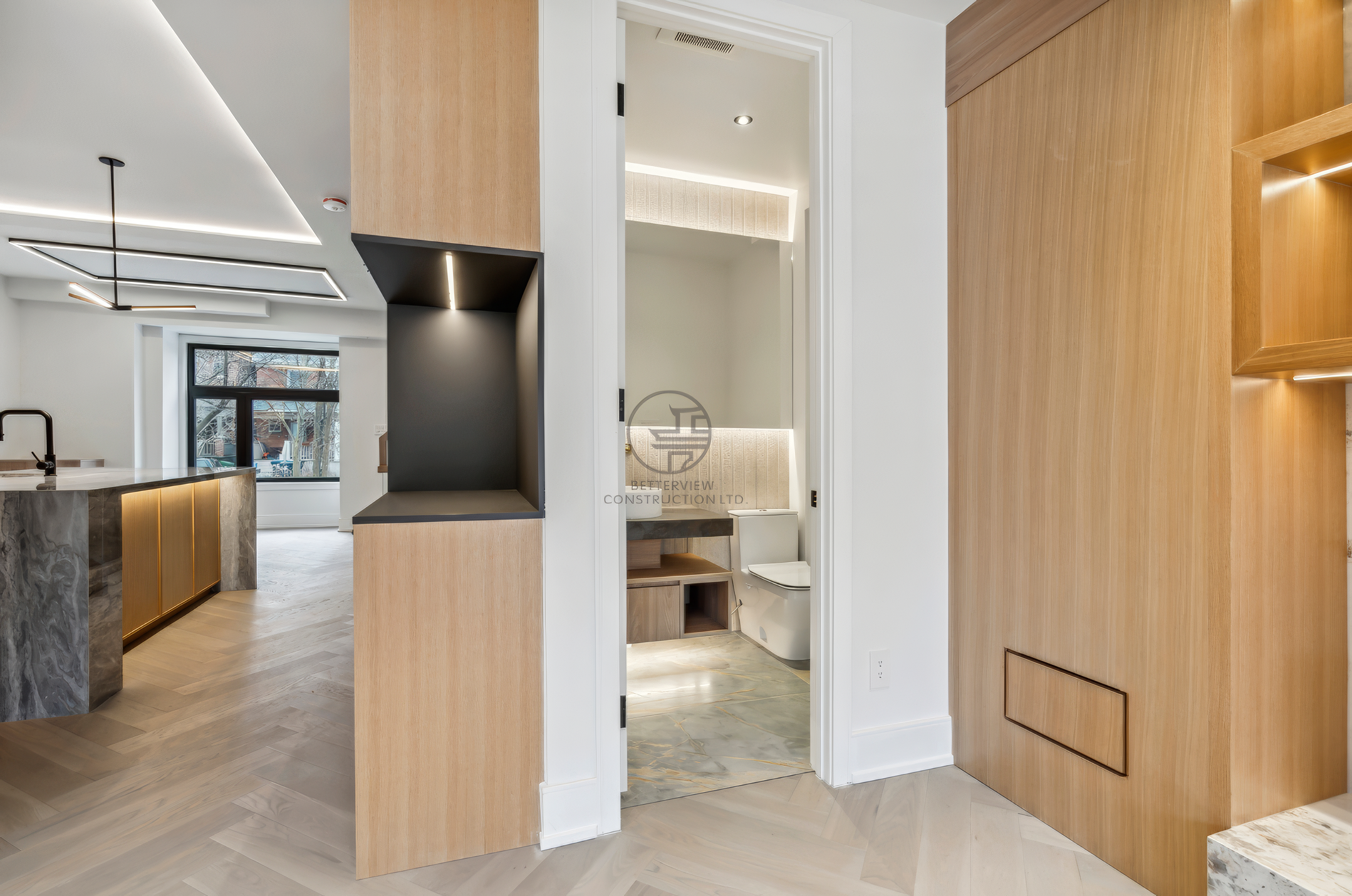 Modern interior hallway connecting open-concept kitchen and powder room with custom wood paneling, built-in storage, and contemporary lighting design.