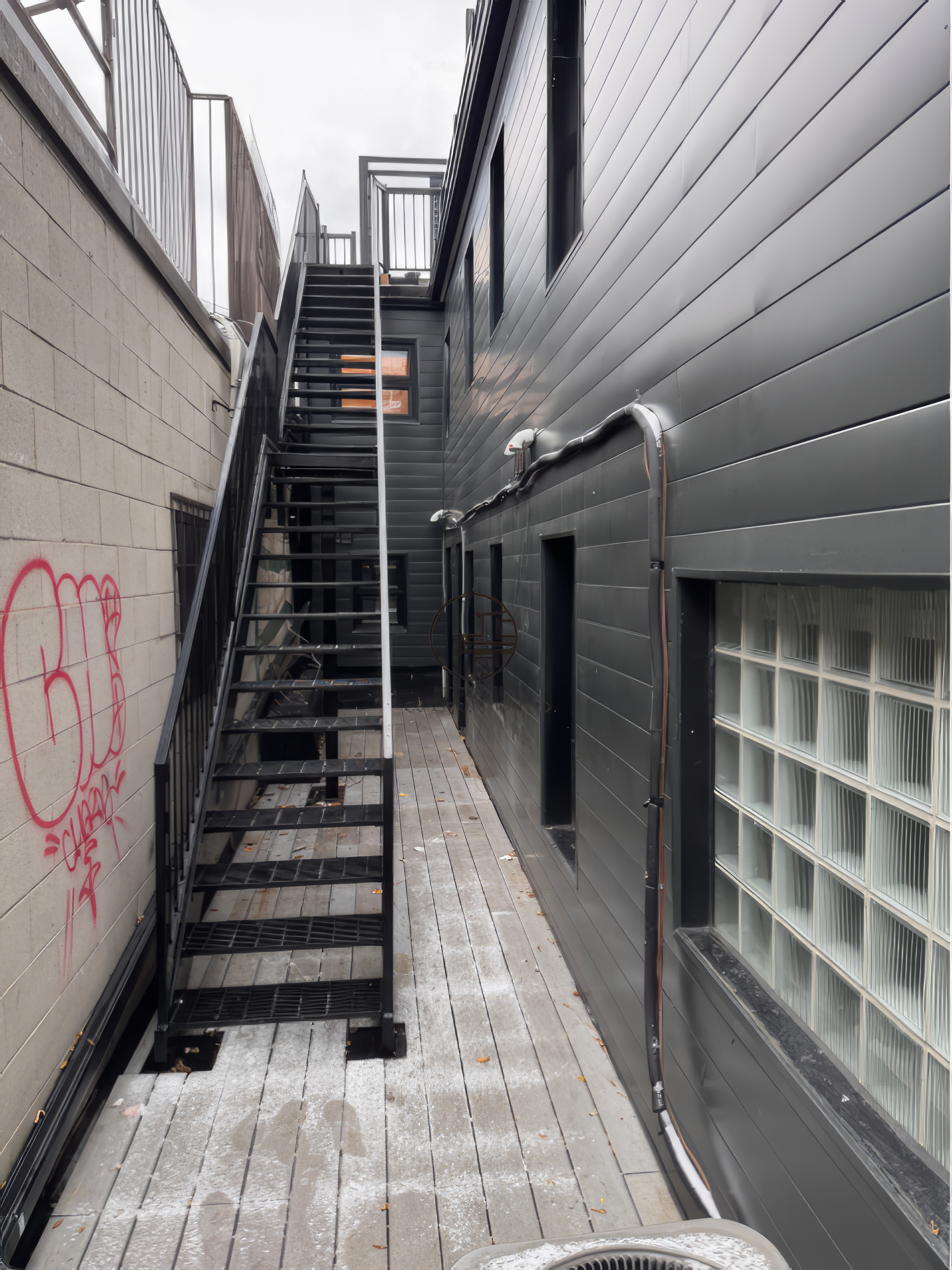 Exterior side yard renovation in Toronto featuring metal staircase, narrow access walkway, and modern siding