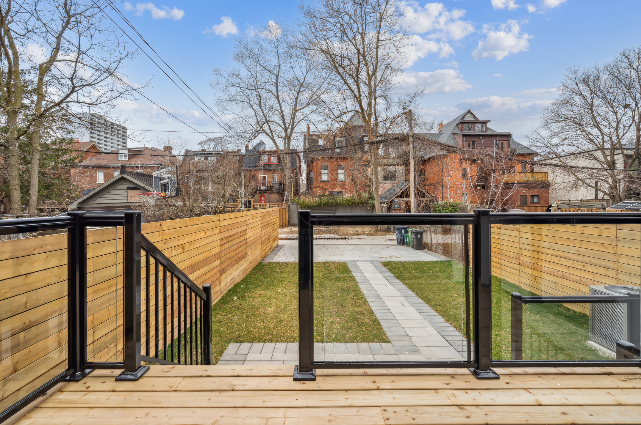 Modern backyard with wooden deck, glass railing, landscaped lawn, and pathway in a residential home renovation project