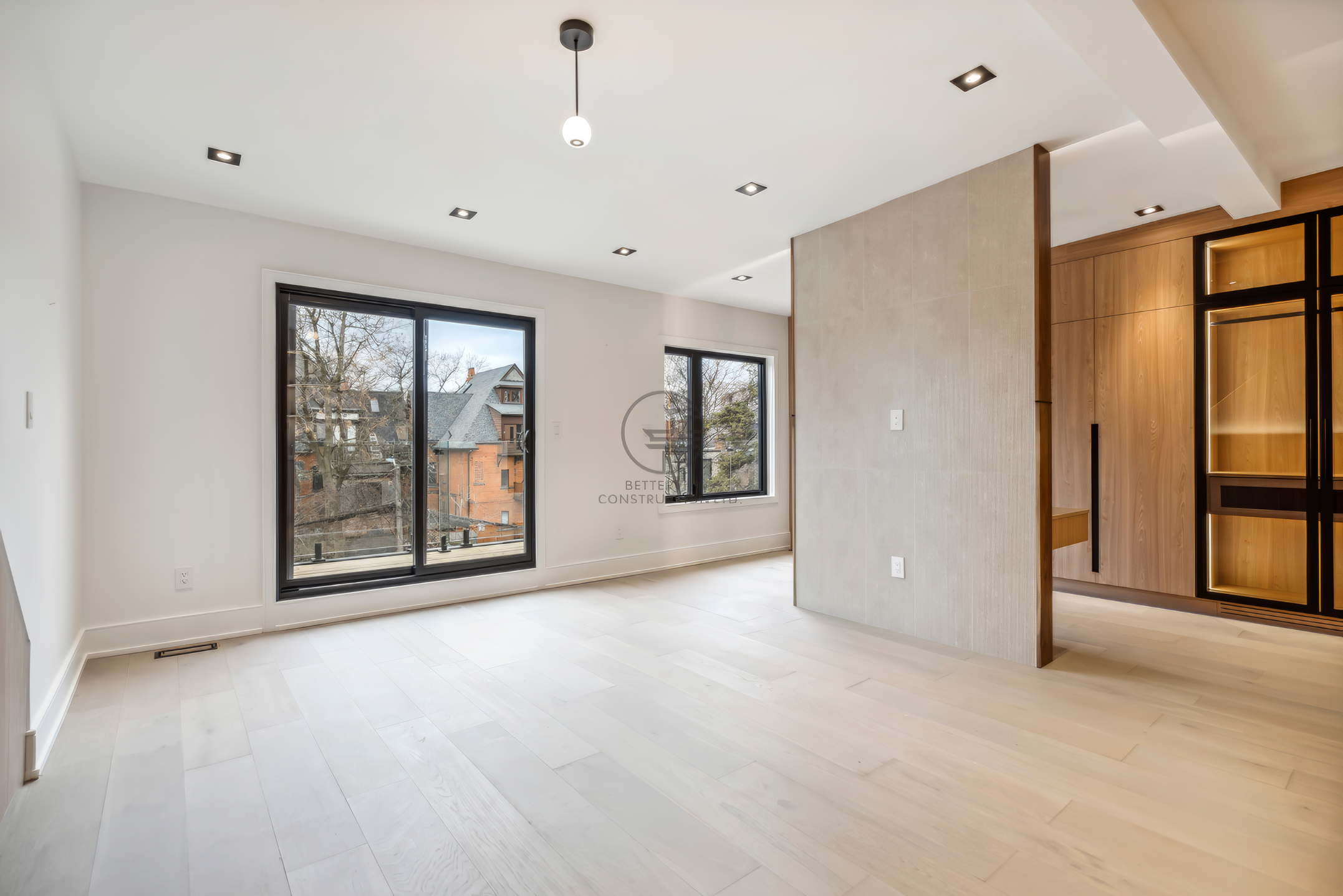 Spacious modern bedroom with large windows, light wood flooring, partial divider wall, and open walk-in closet with built-in shelving and lighting.