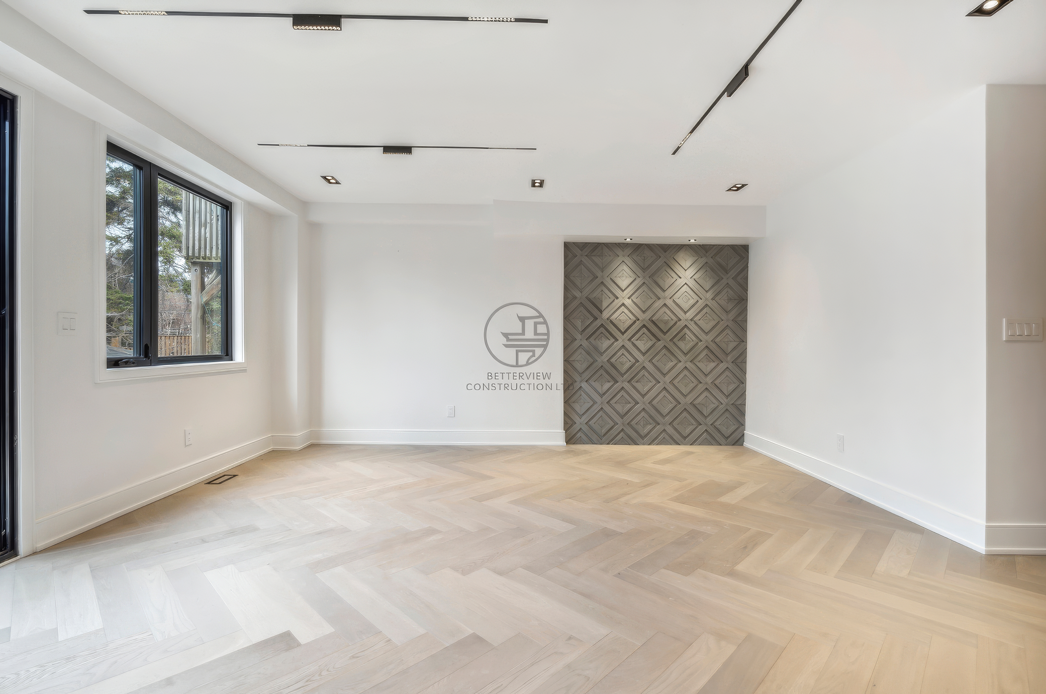 Modern living room with herringbone wood flooring, large window, recessed ceiling lighting, and decorative feature wall with geometric pattern.