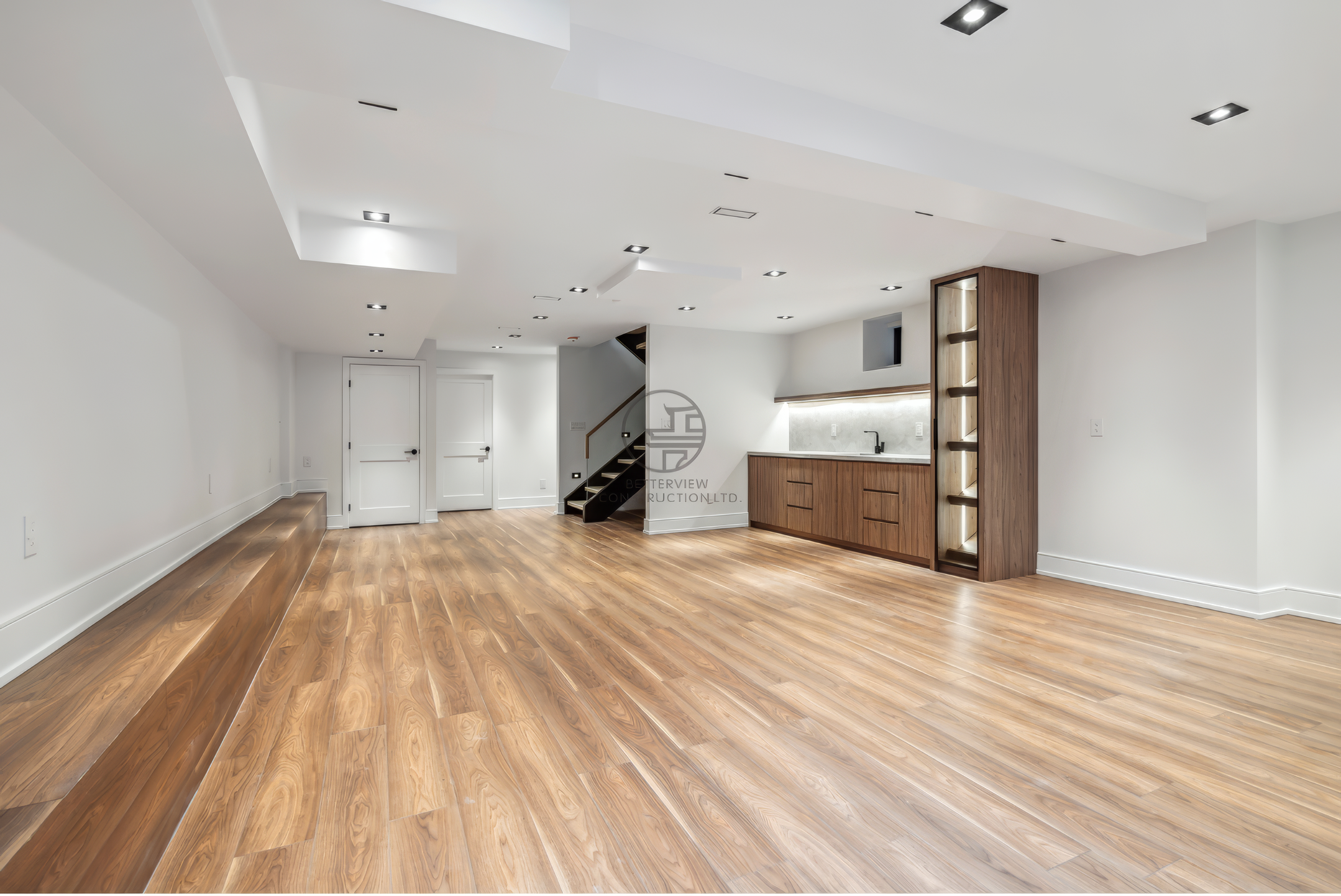 Spacious finished basement with wood flooring, recessed lighting, built-in cabinets, and open-concept design in a residential home renovation project