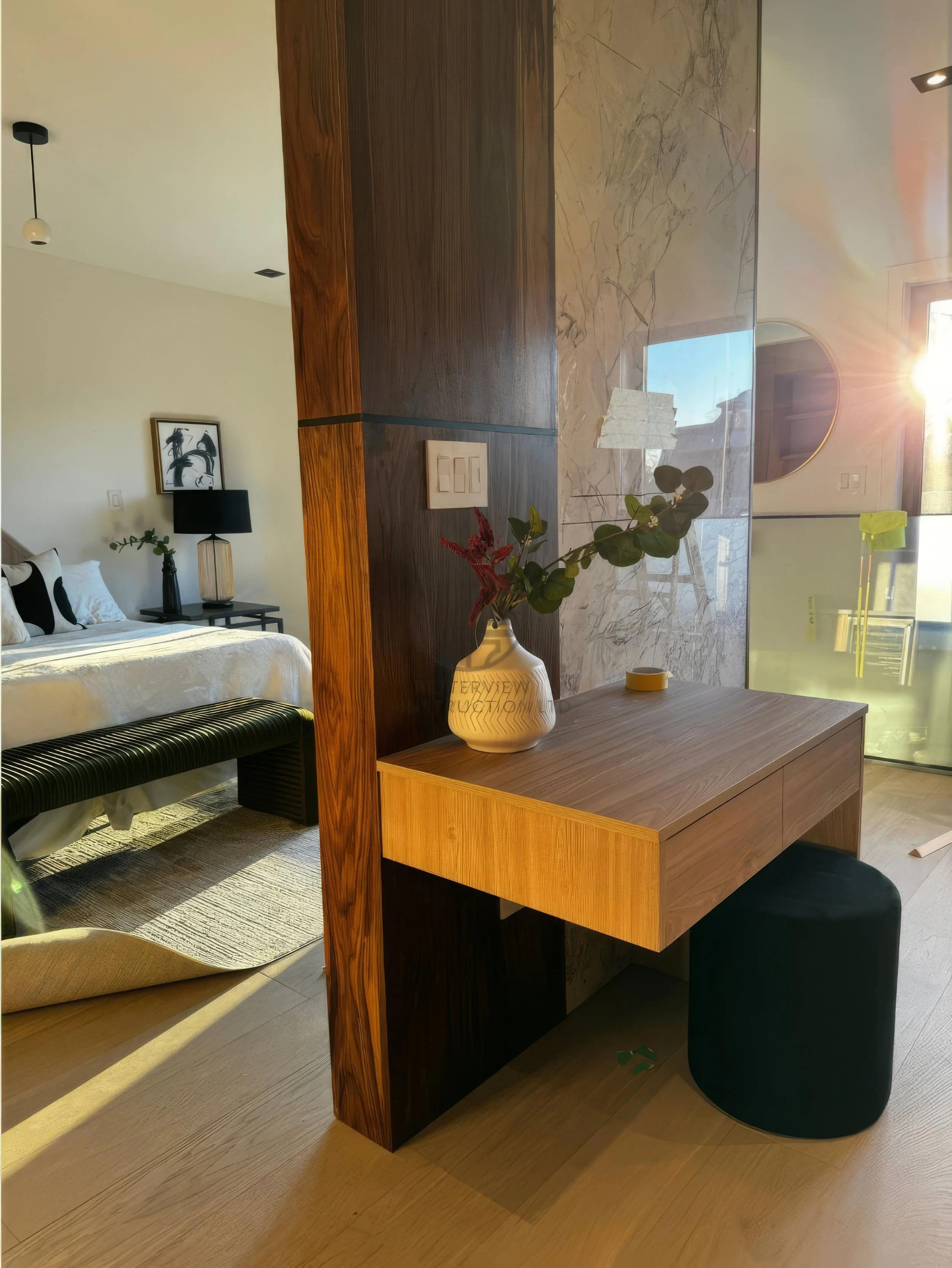 Modern bedroom design with wood partition wall, floating desk vanity, upholstered stool, and minimalist decor with warm natural lighting.