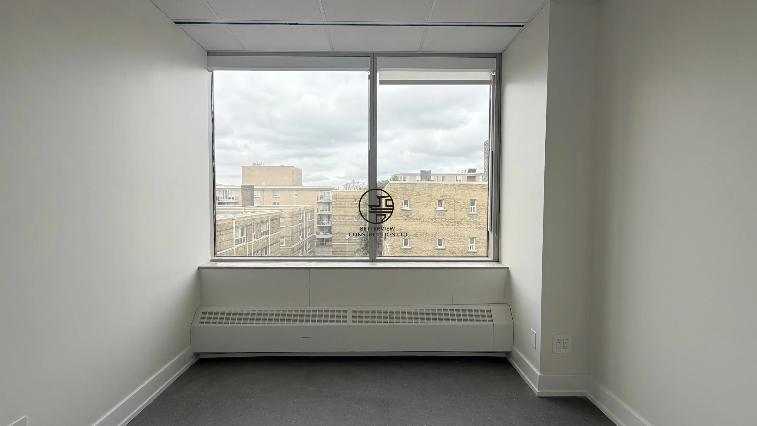 Small office room with large window, carpet flooring, and minimalist interior in commercial renovation
