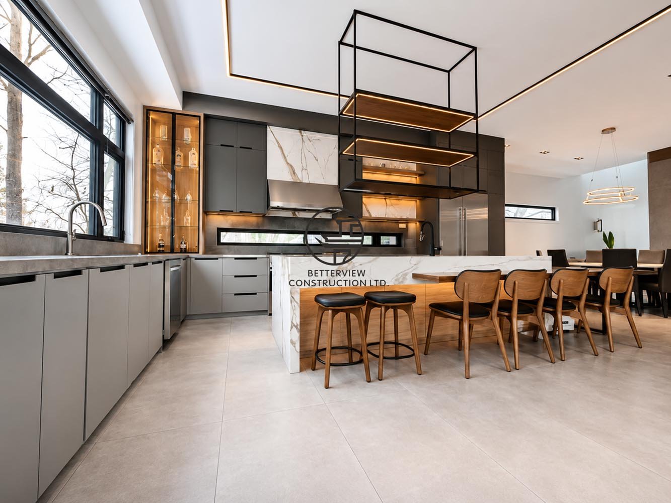 Modern open-concept kitchen with large island, LED ceiling lighting, grey cabinetry, and integrated dining area with wooden chairs and pendant lighting.