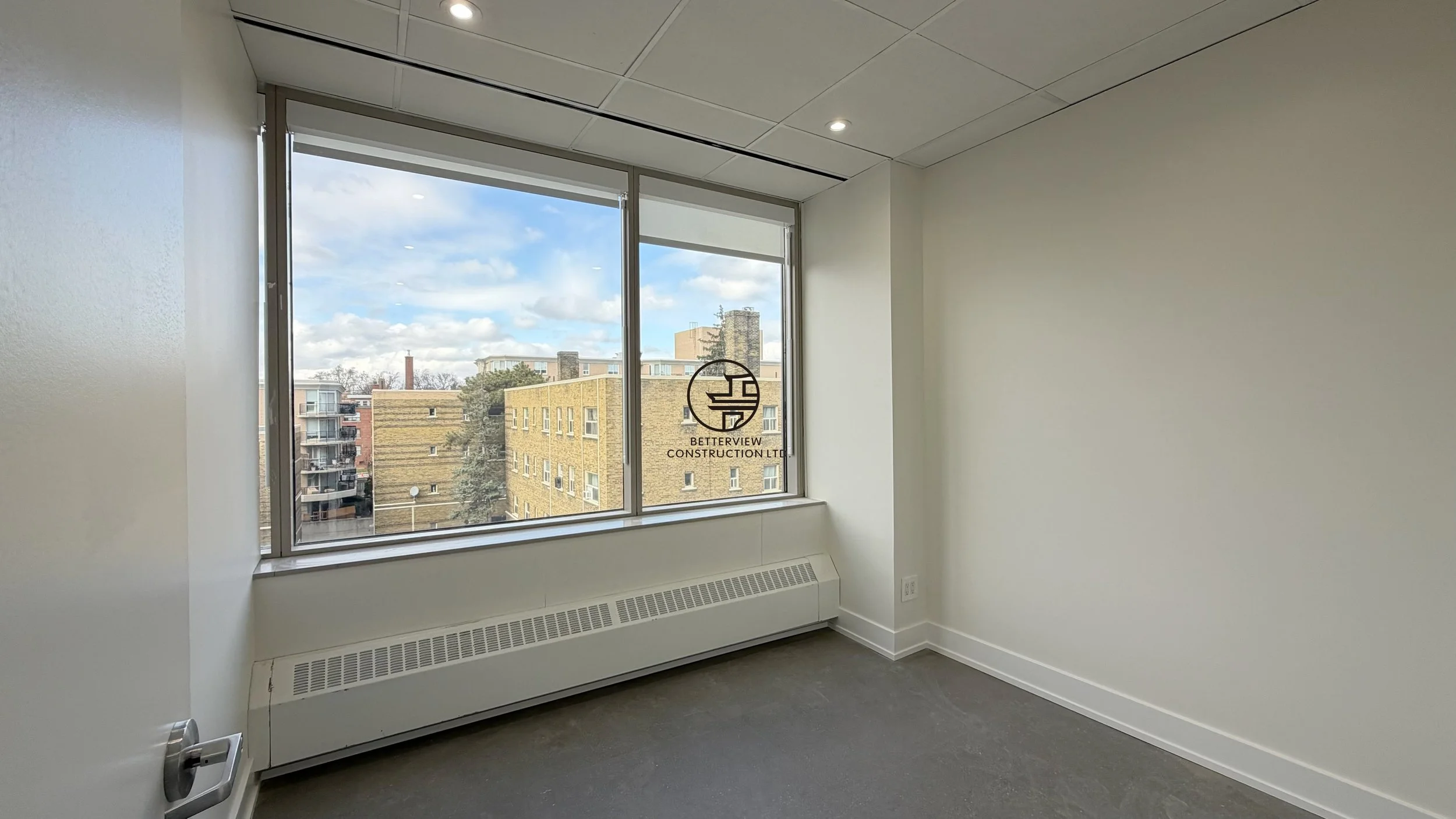 Private office room with large window, natural light, and carpet flooring in modern commercial renovation