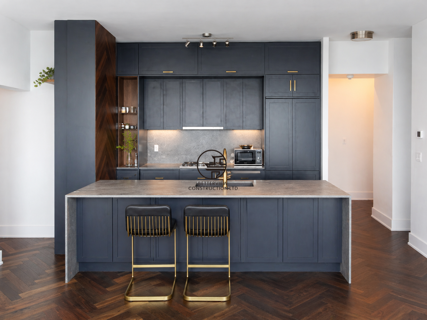 Modern kitchen with dark cabinetry, large island, pendant lighting, and herringbone wood flooring in an open-concept living space.