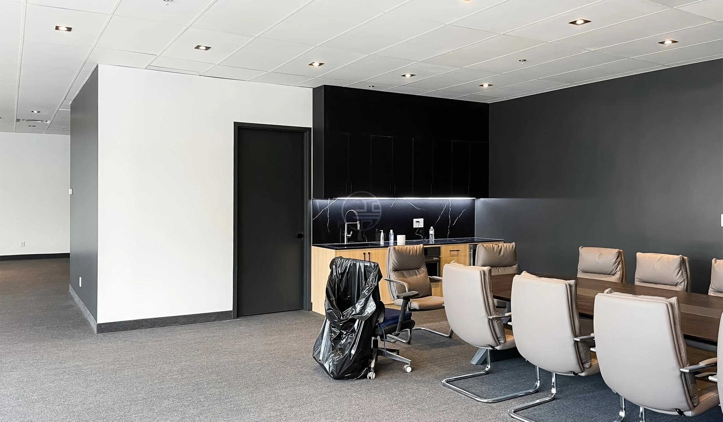 Modern office breakroom and kitchenette renovation in Toronto featuring black cabinetry, marble backsplash, and integrated meeting space
