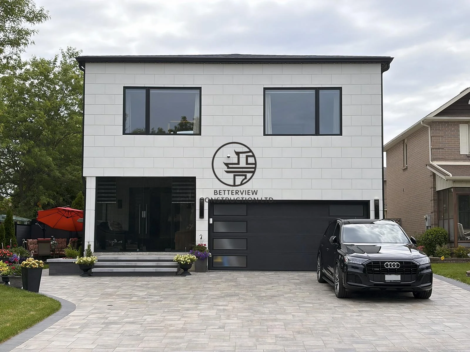 This modern home addition features a clean white exterior, expansive black-framed windows, and a contemporary garage façade, creating a seamless extension that enhances both curb appeal and functionality.