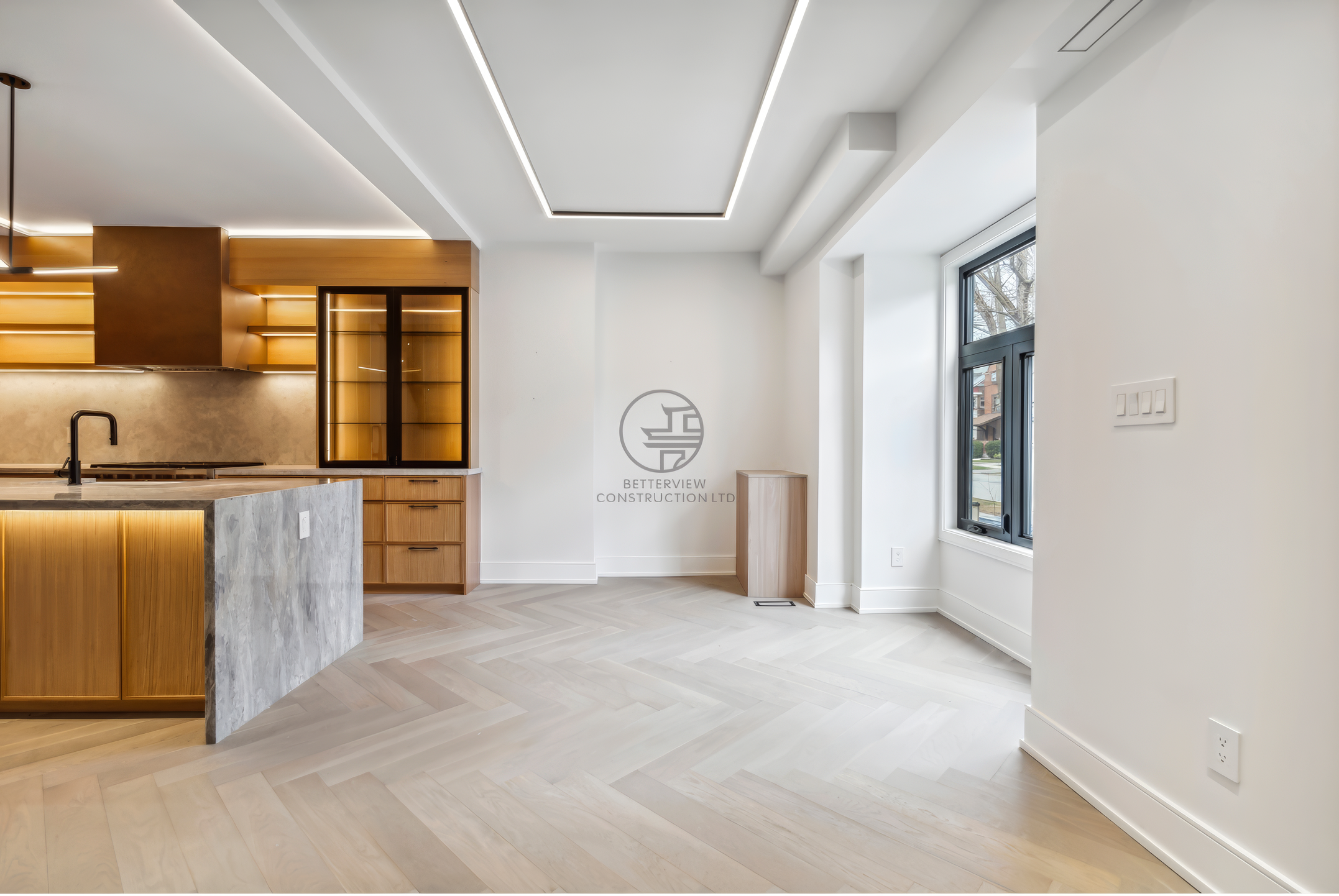Bright open-concept kitchen and living space with herringbone wood flooring, marble island, wood cabinetry, and recessed LED ceiling lighting.