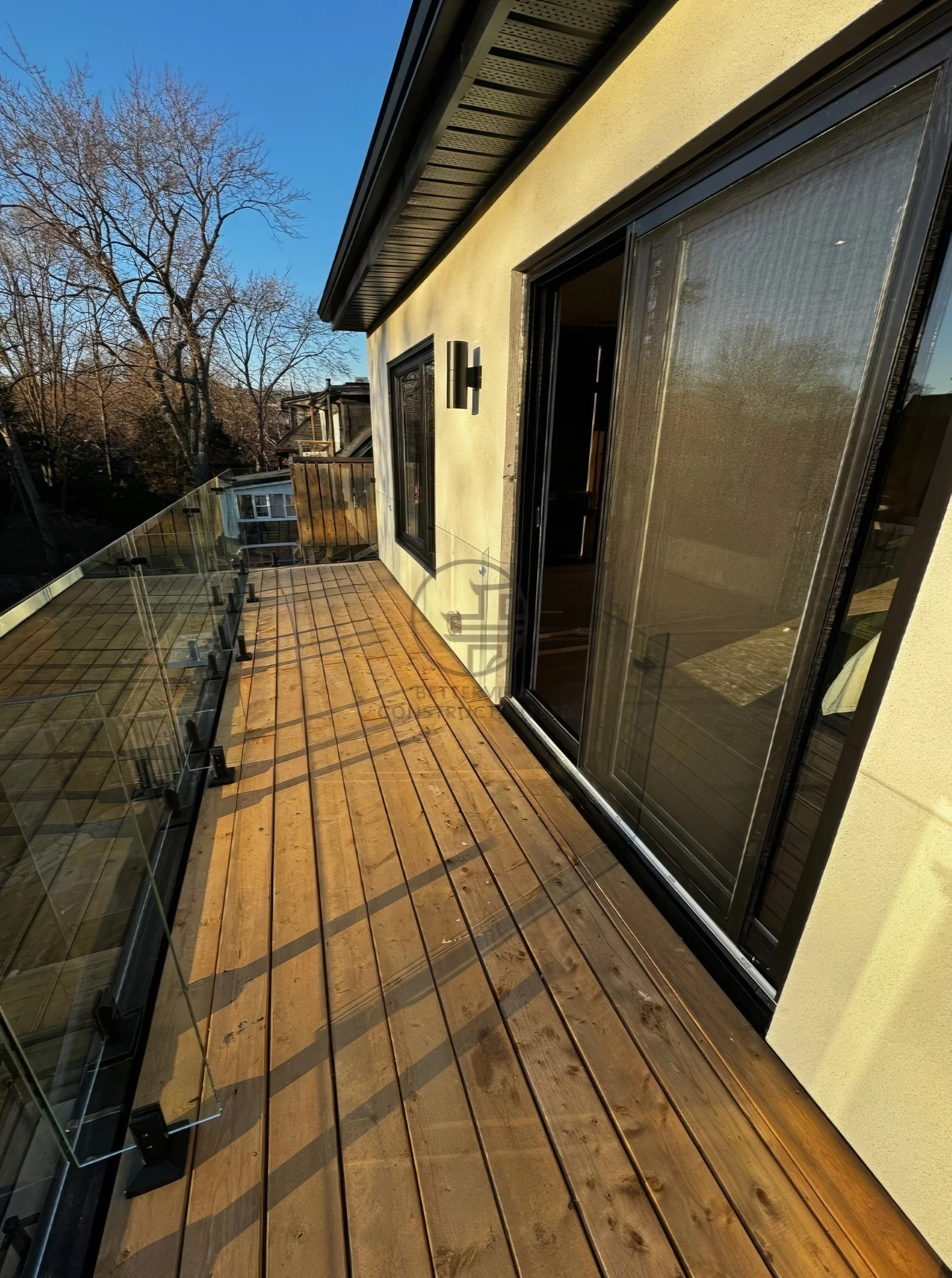 Modern balcony with wood deck flooring, glass railing, sliding glass doors, and outdoor view in contemporary home design.