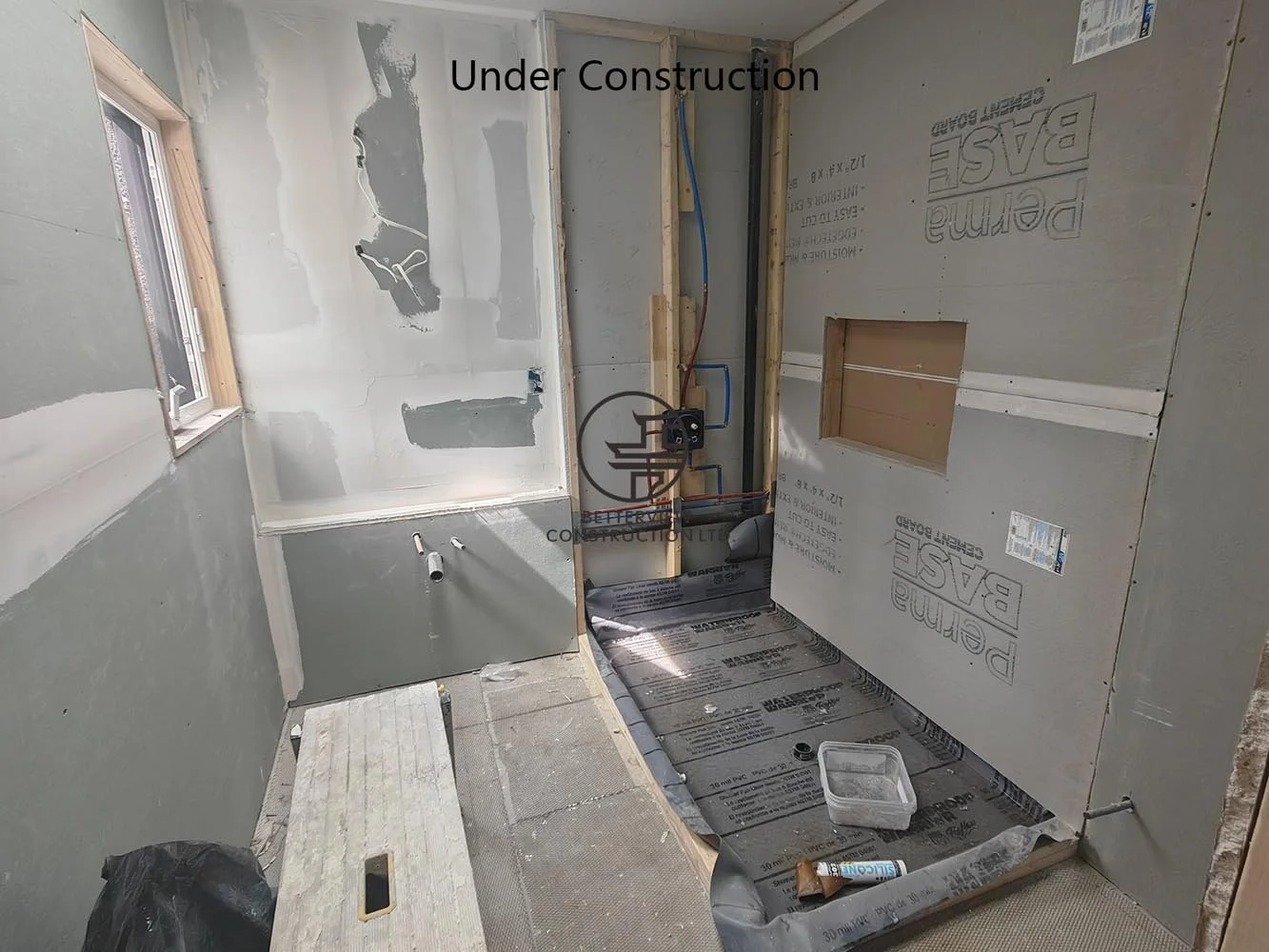 Bathroom under construction featuring plumbing rough-ins, waterproofing preparation, and a walk-in shower before final tile installation.