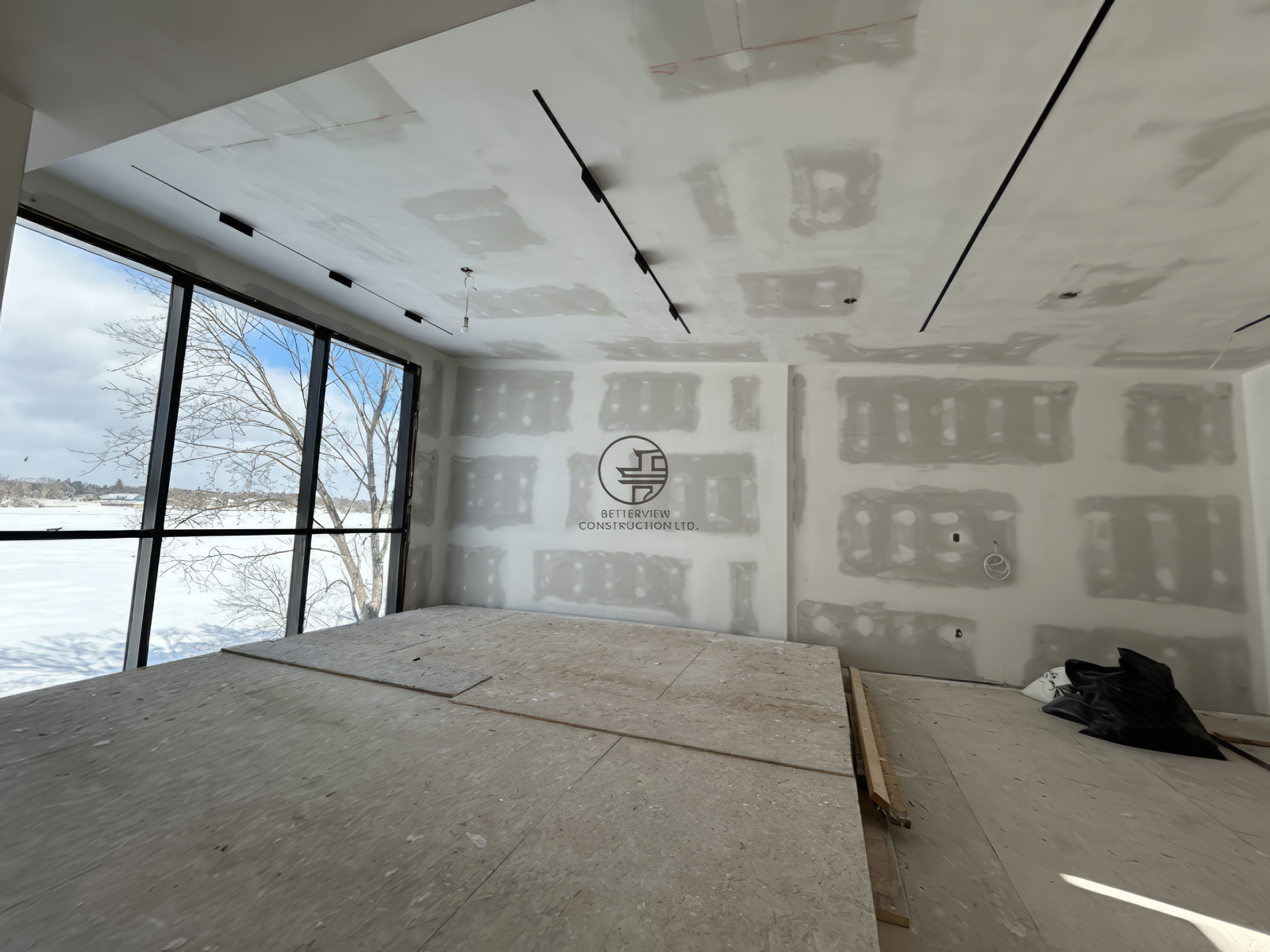 Open concept interior renovation with drywall finishing and large windows, modern living space under construction