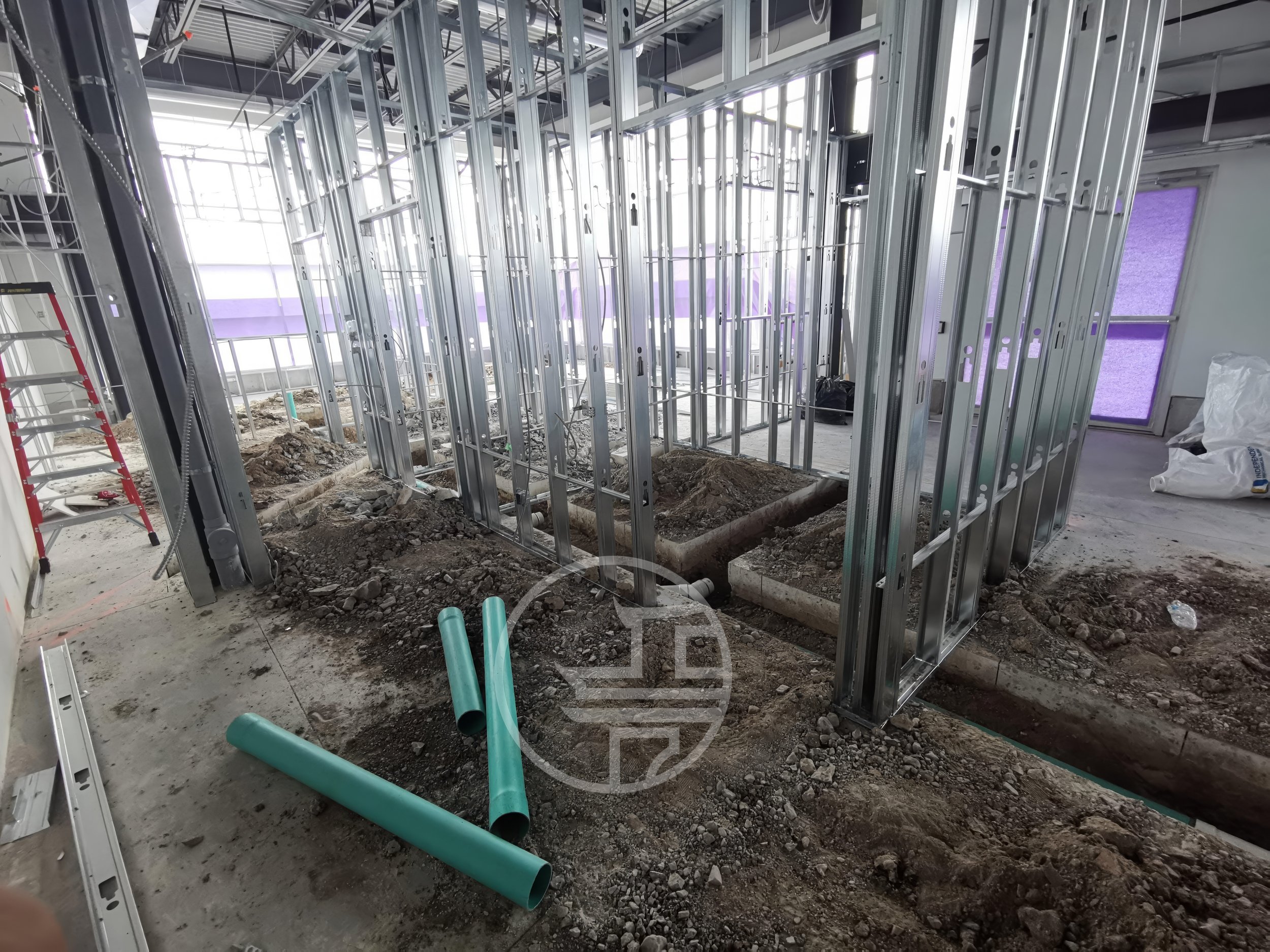 Commercial interior build-out with plumbing trenching, drainage pipe installation, and steel stud framing during construction 