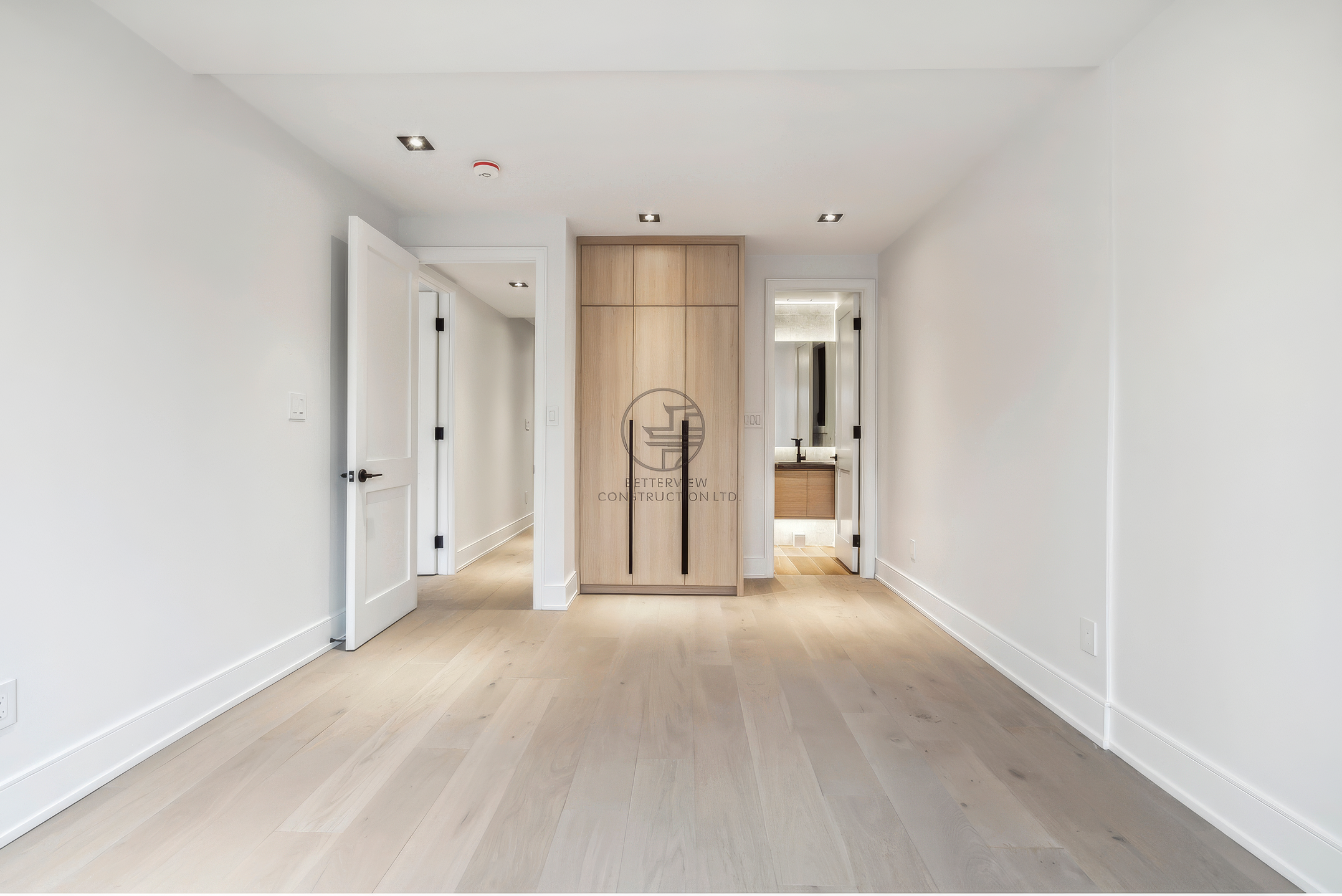 Minimalist bedroom with light wood flooring, built-in closet with wood panel doors, recessed lighting, and clean white walls in modern home design.