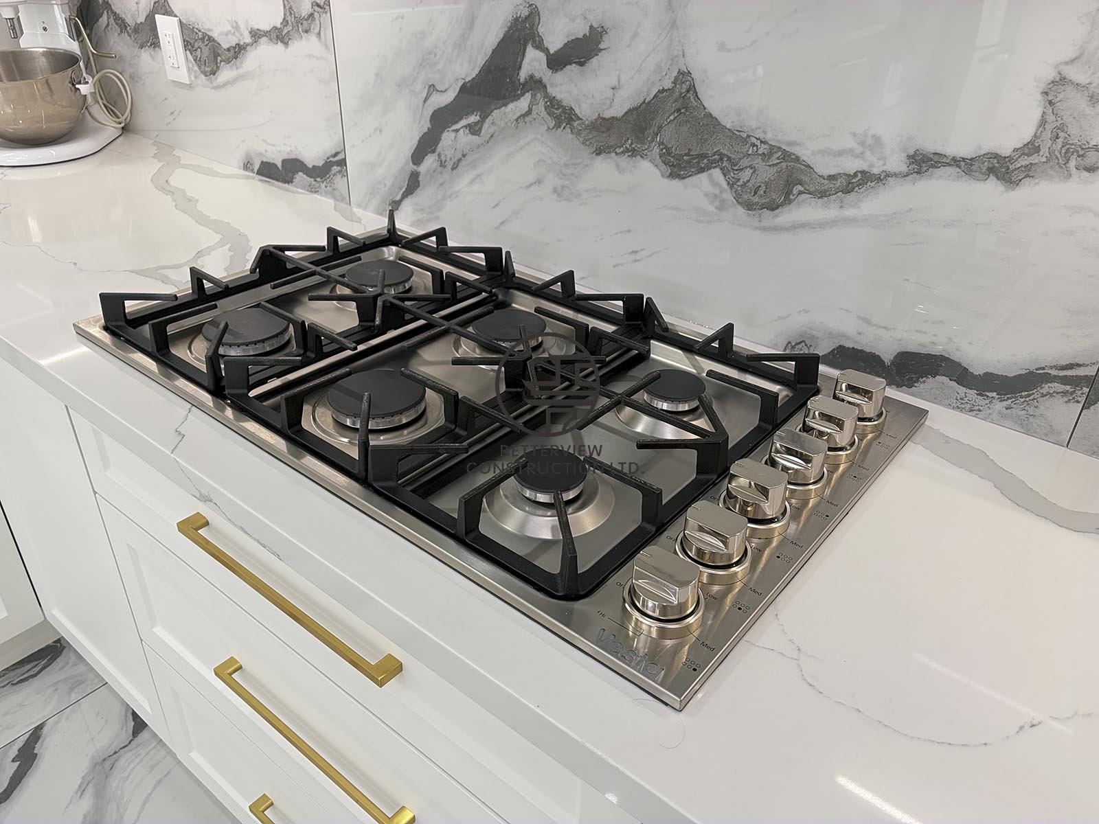 Premium stainless steel gas cooktop with quartz countertops and a full-height marble-look backsplash delivers professional performance while enhancing the kitchen's modern design.