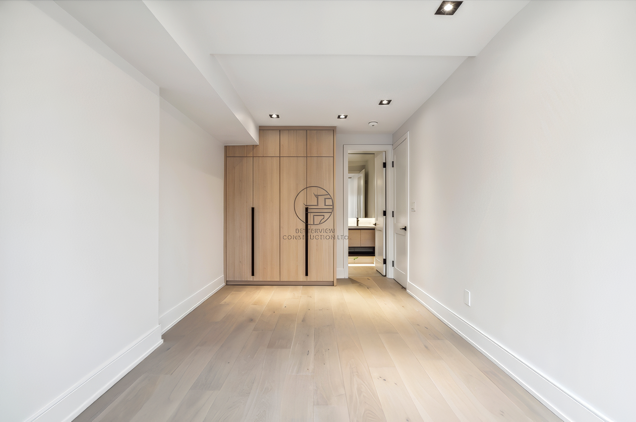 Minimalist bedroom with light wood flooring, built-in wardrobe with sleek handles, recessed ceiling lighting, and clean modern interior design.