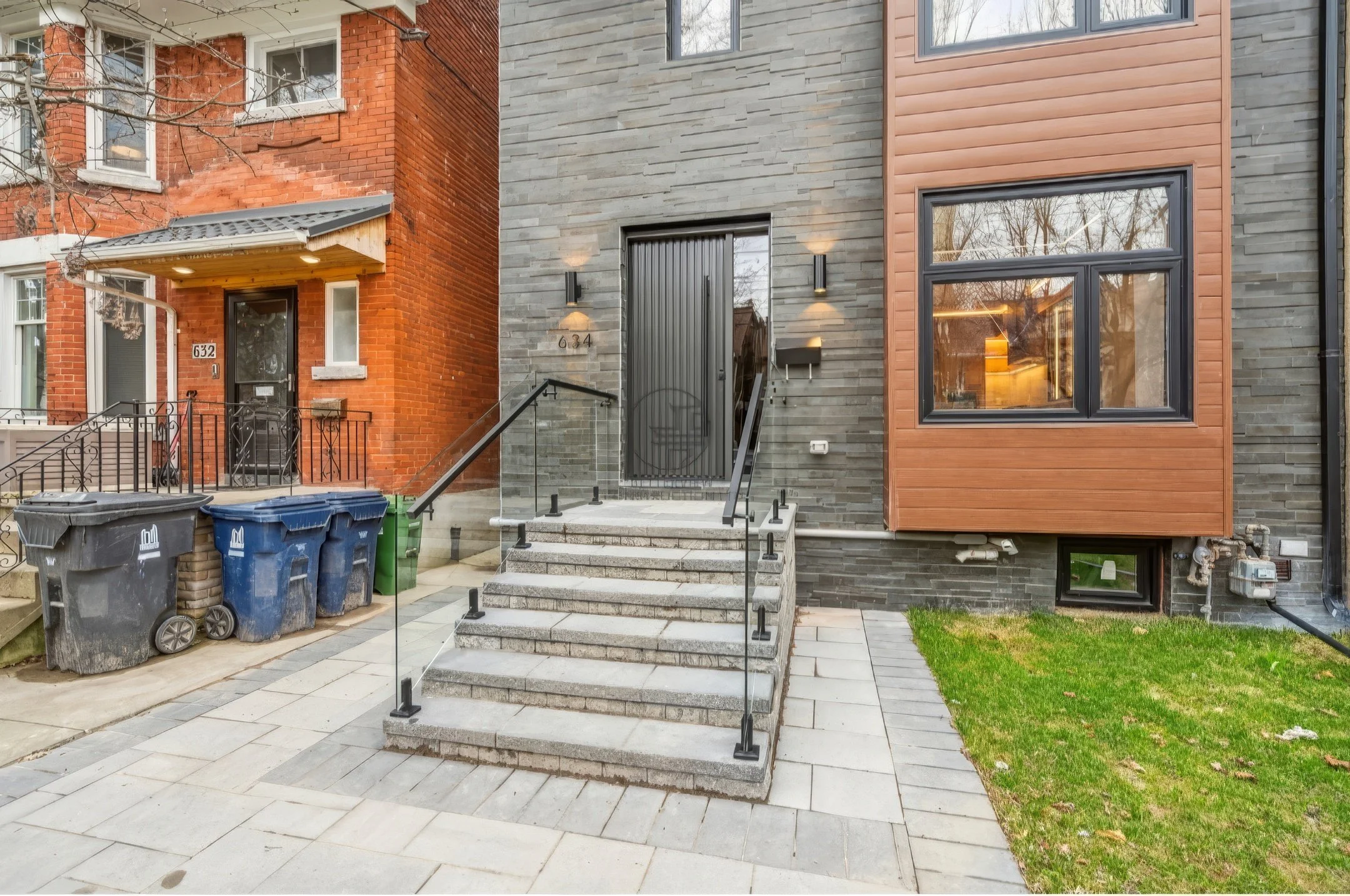 Modern home exterior with stone facade, front steps with glass railing, contemporary door, and mixed brick and wood siding design.