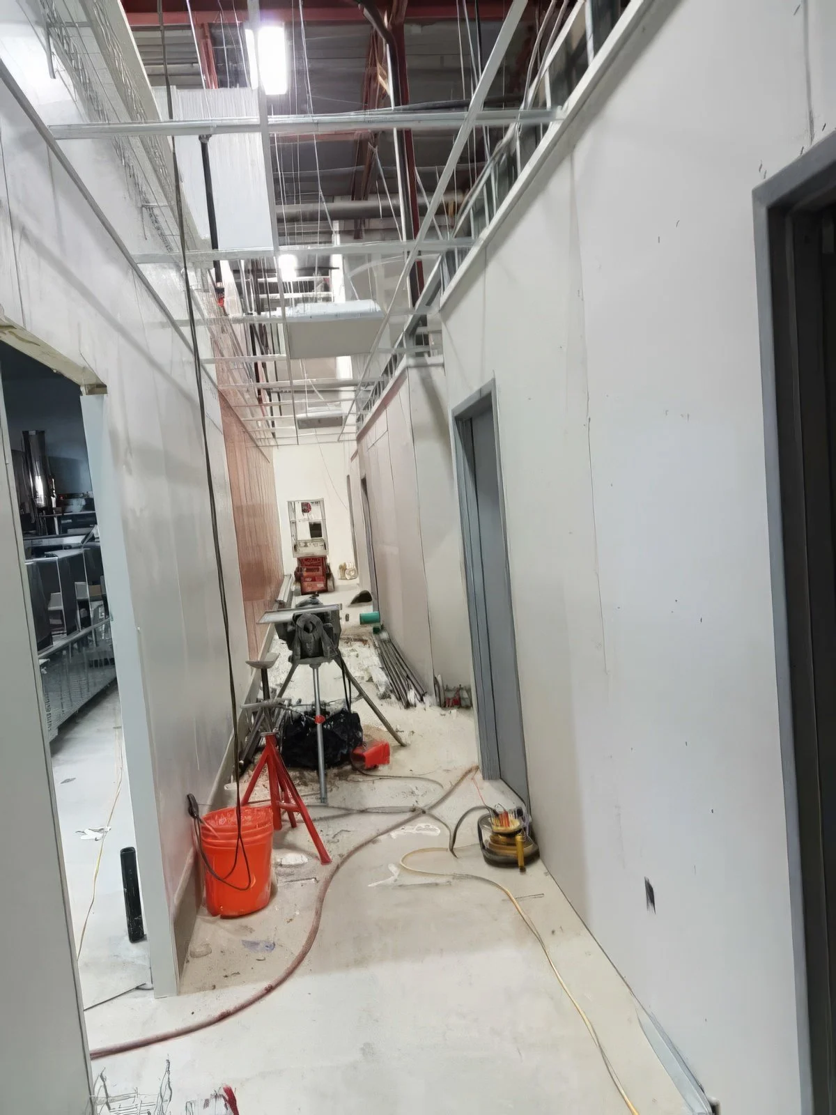 Commercial corridor under active construction with drywall walls, ceiling grid installation, and ongoing renovation work in a Toronto warehouse project