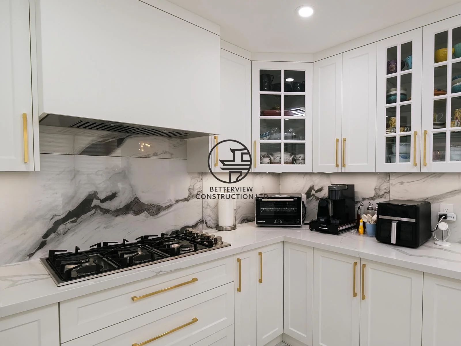 The custom kitchen cooking area features a professional gas cooktop, concealed range hood, full-height marble-look backsplash, and custom cabinetry designed for a clean, luxurious finish.