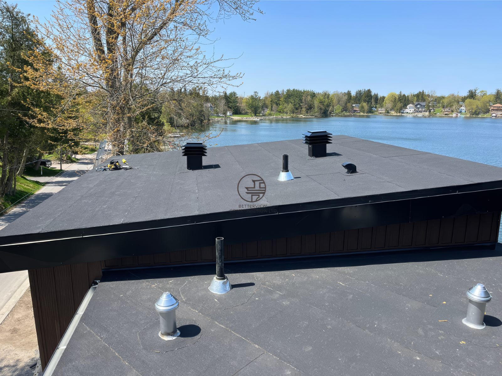 Flat roof installation on modern home with rooftop vents and waterfront view, exterior construction nearing completion