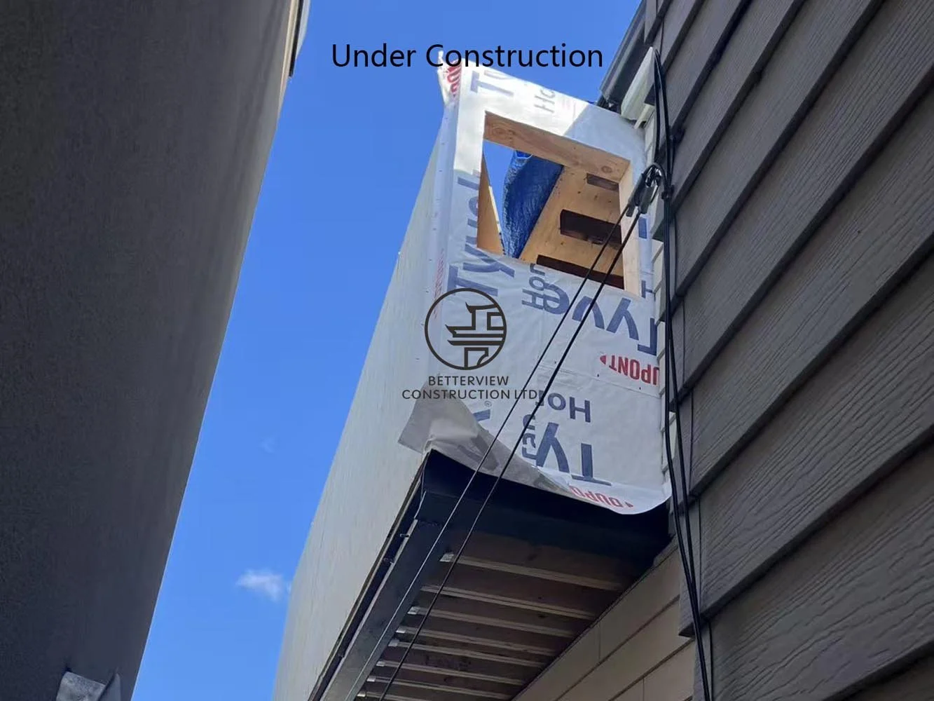 Cantilevered second floor under construction featuring exterior sheathing, structural framing, and preparation for the modern stucco façade.