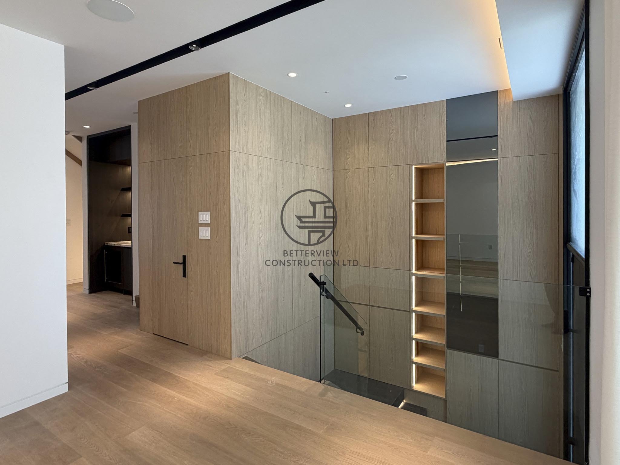 Modern interior with custom built-in wood cabinetry, shelving niche and staircase glass railing