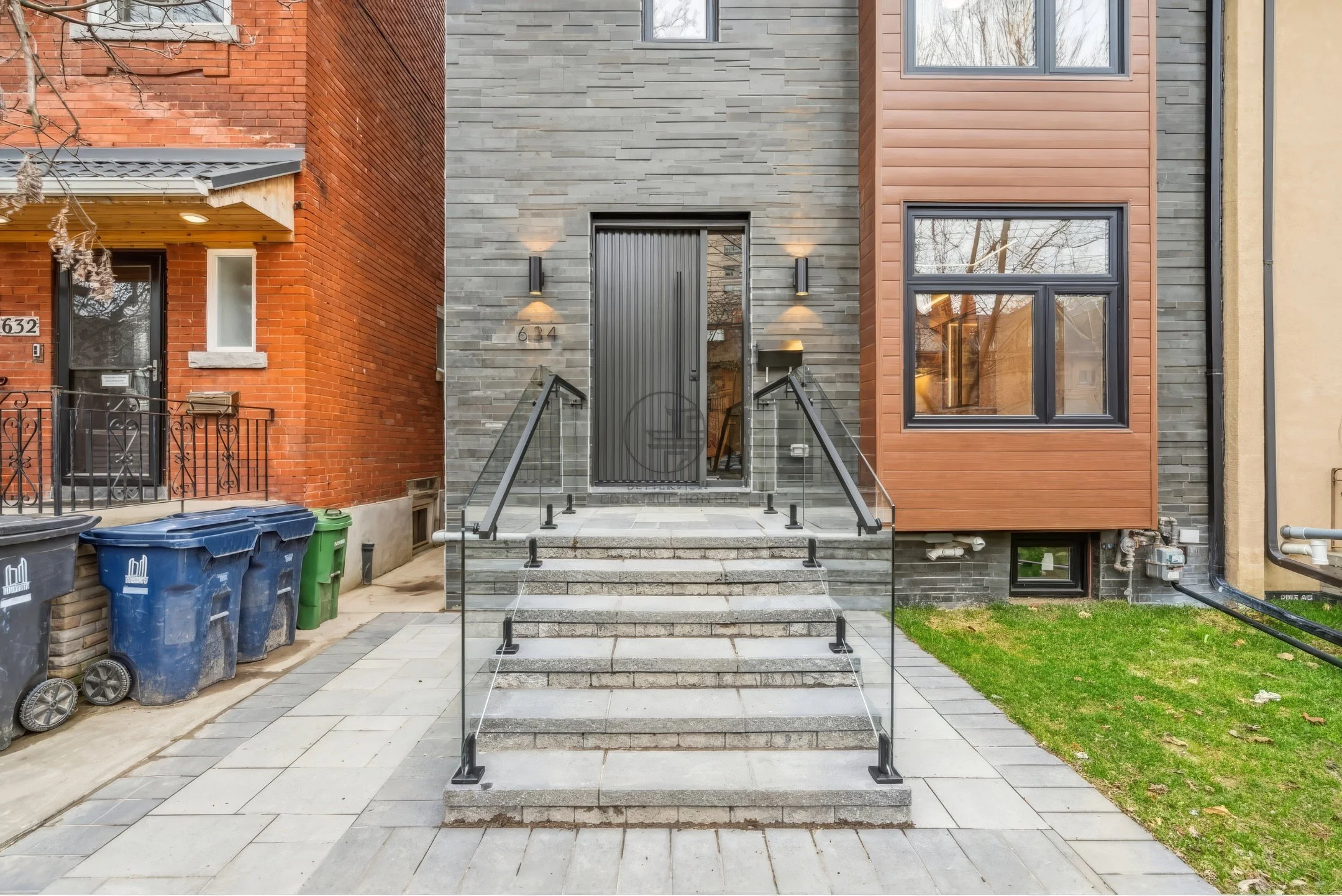 Contemporary home front entrance with stone steps, glass railing, modern front door, and mixed brick and wood exterior facade.
