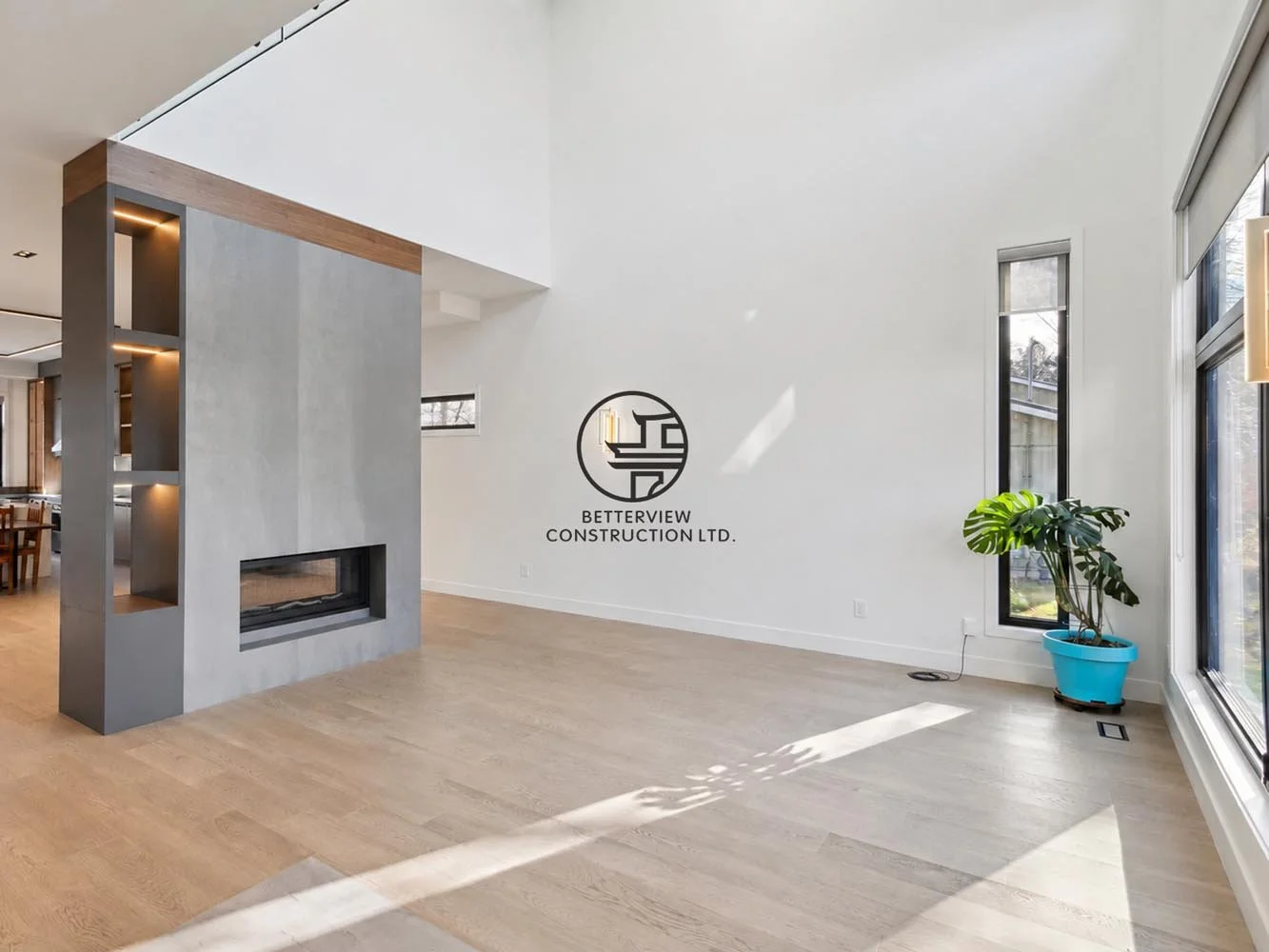 Modern living room with built-in fireplace feature wall, open-concept layout, large windows, light wood flooring, and bright natural sunlight.
