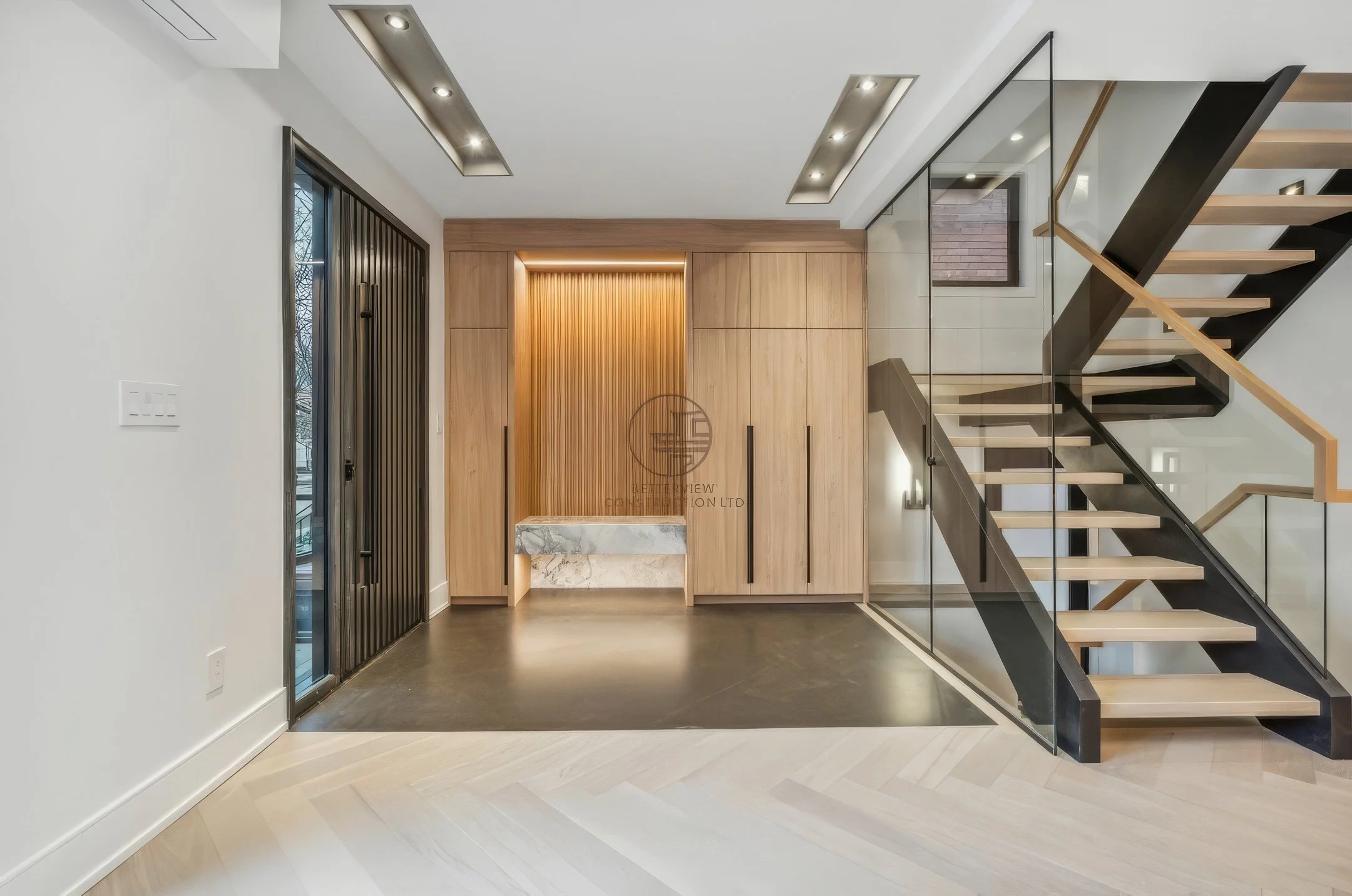 Modern entryway design with floating staircase, glass railing, wood panel wall with built-in storage, and integrated bench with accent lighting.