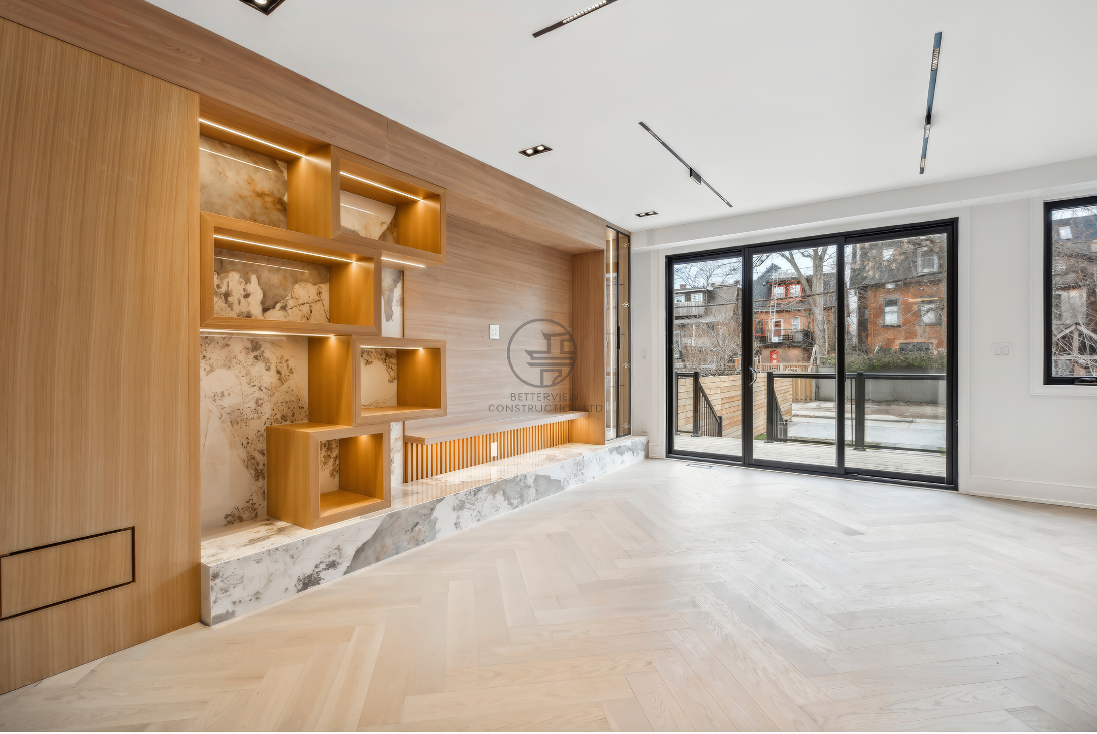 Modern living room with wood feature wall, built-in shelving with lighting, herringbone wood flooring, and large sliding glass doors.
