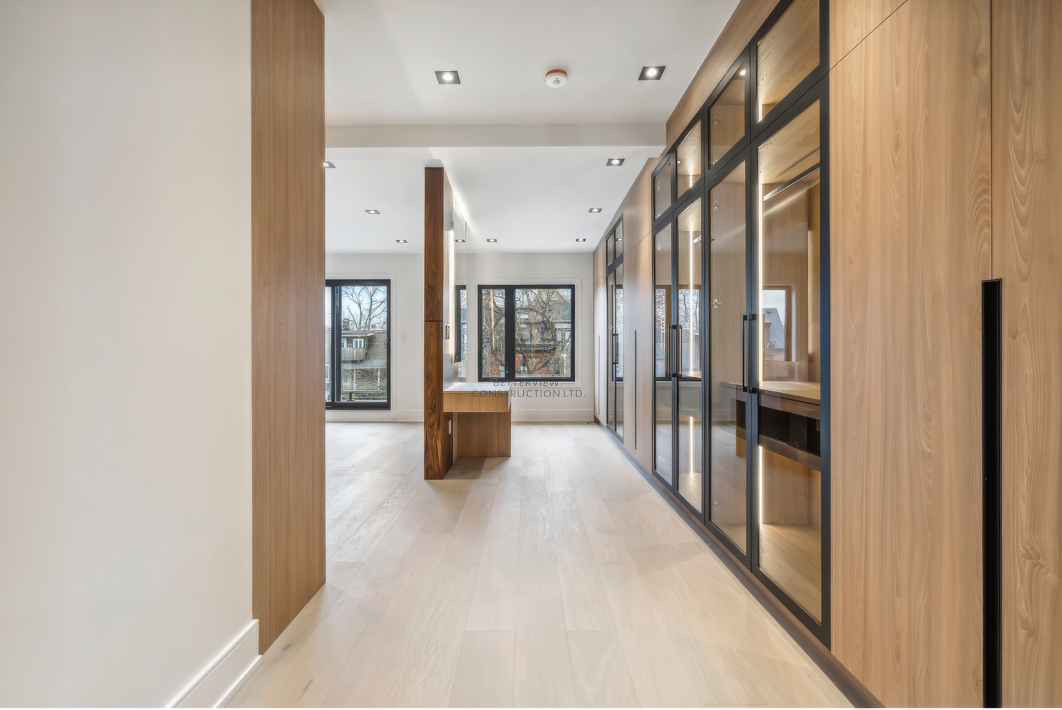 Modern hallway with custom wood paneling, glass partition walls, built-in cabinetry, and recessed lighting in a high-end home renovation project